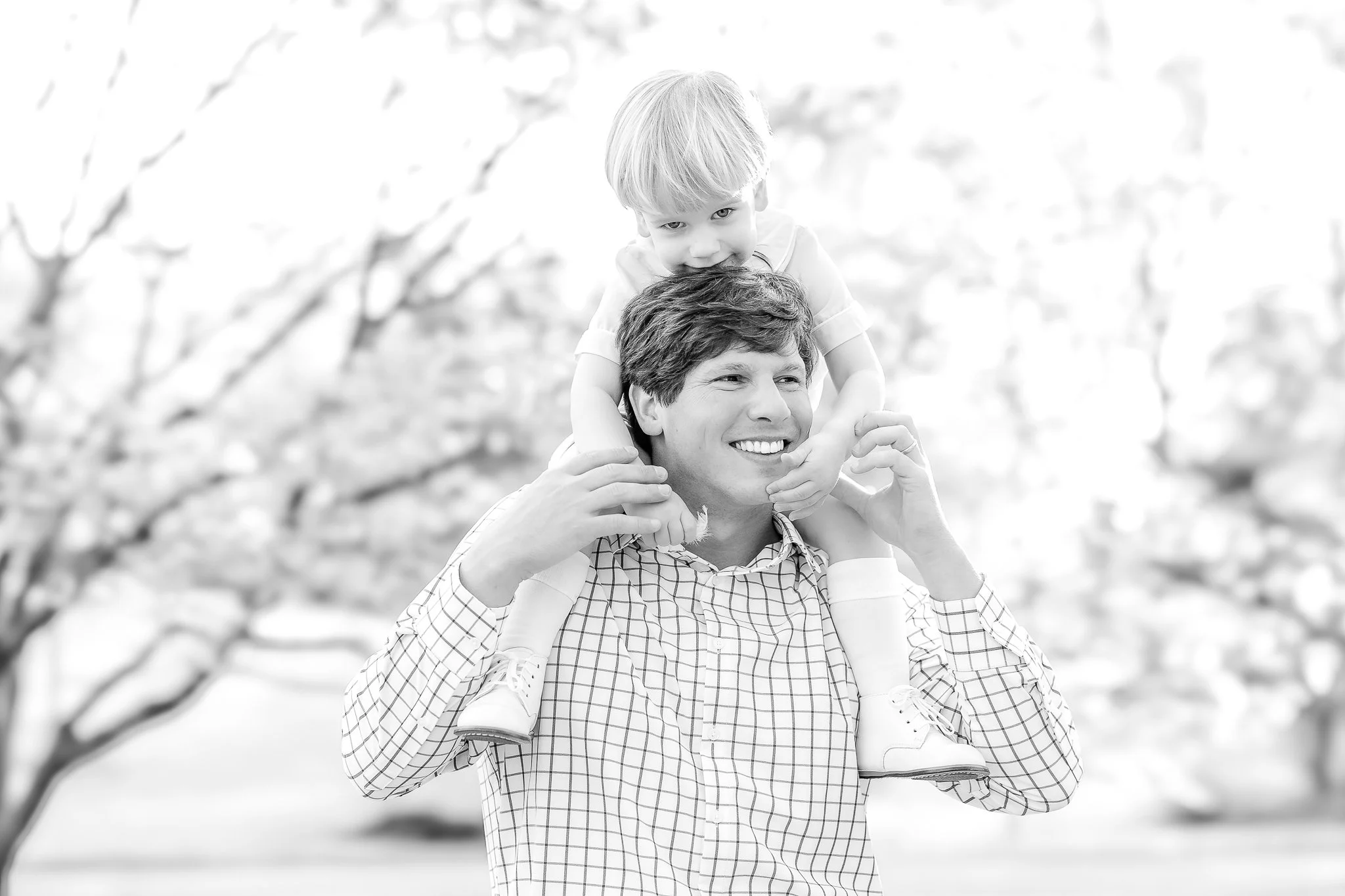 Black and white photo of a smiling man carrying a child on his shoulders outdoors.