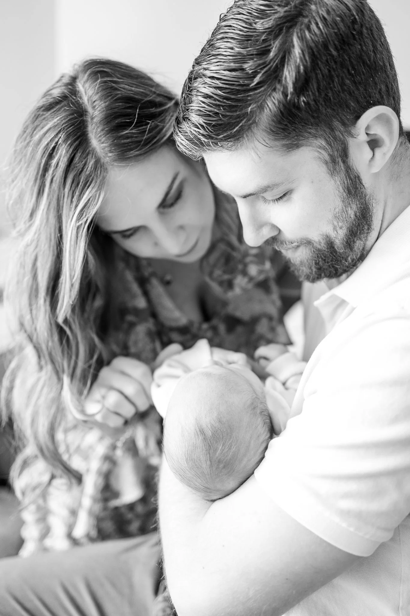 Black and white photo of a couple lovingly gazing at a newborn baby, who is cradled in the man's arms.