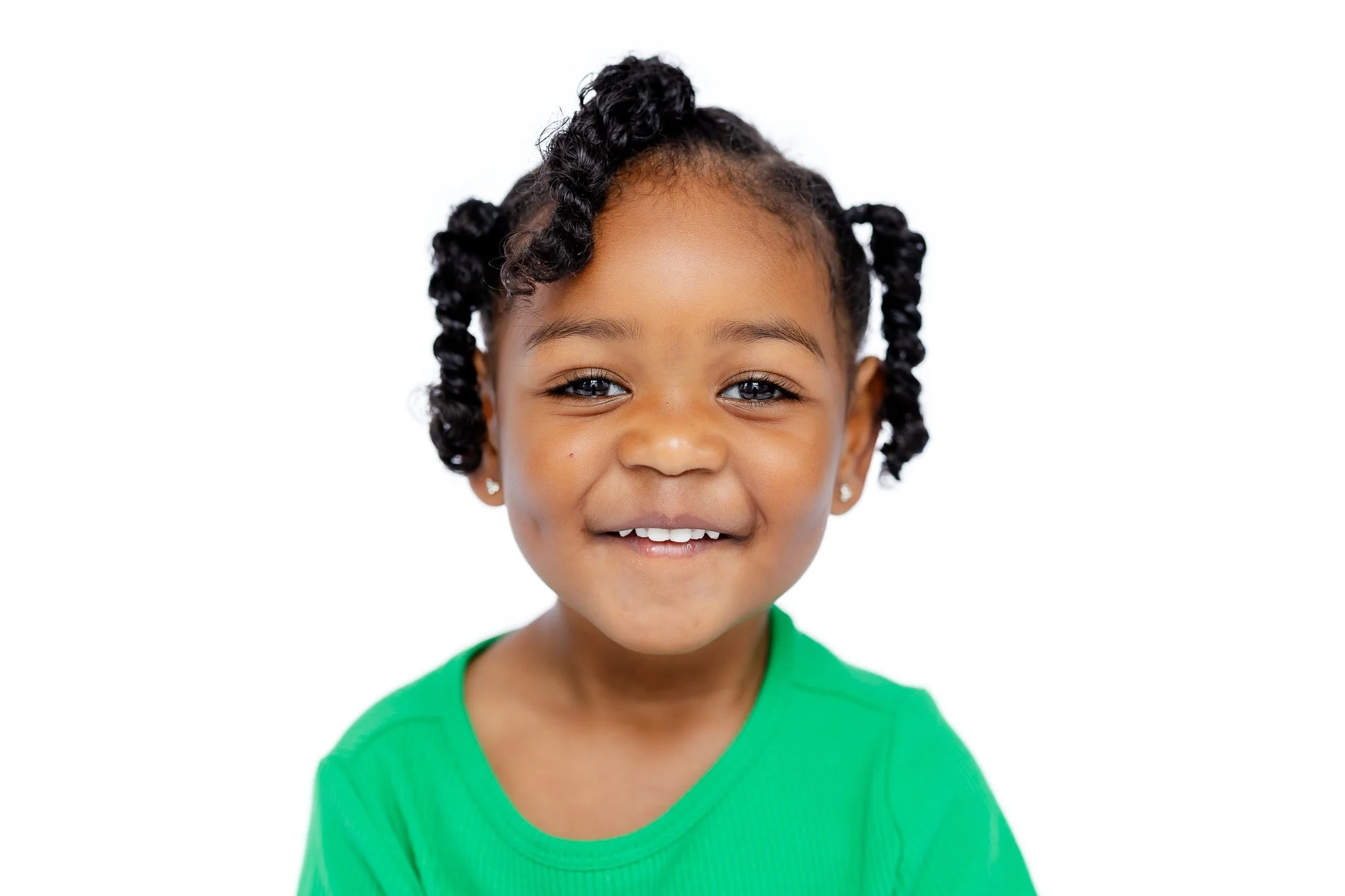 Smiling child with curly hair wearing a green shirt against a white background.