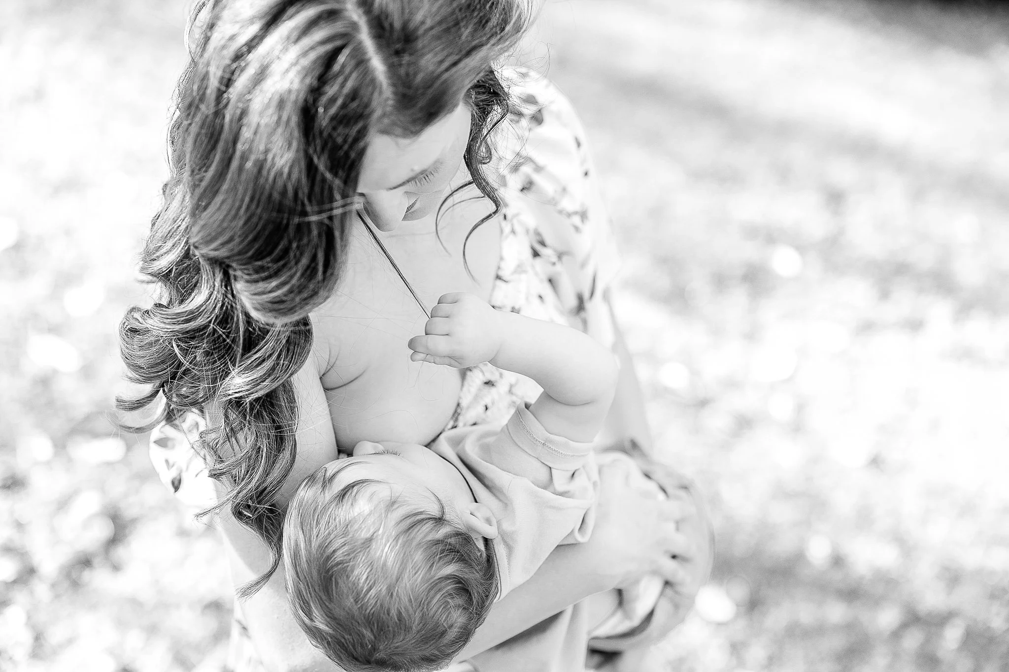 Black and white photo of a woman breastfeeding a baby outdoors.