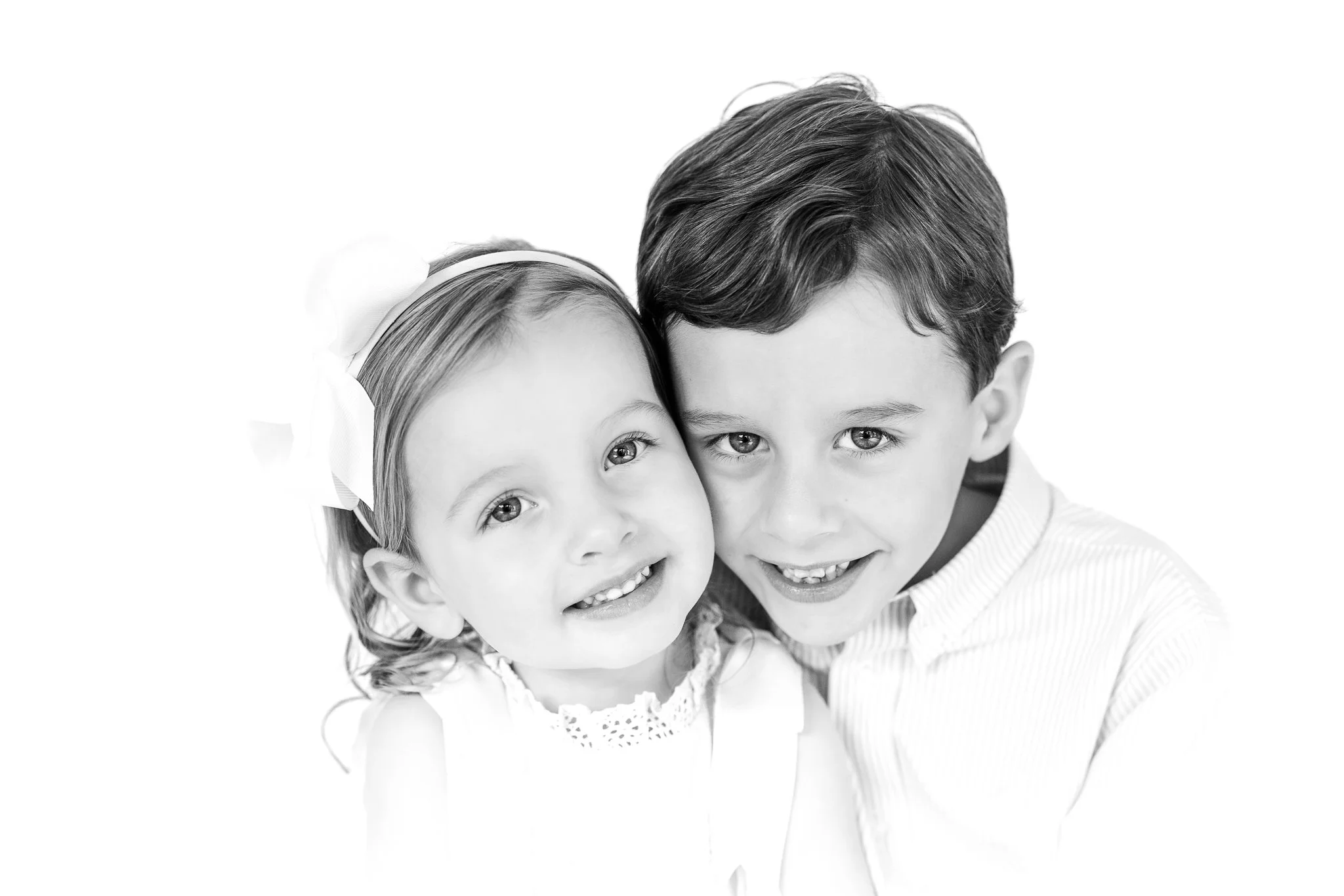 Black and white portrait of two smiling children, a girl with a headband and a boy in a collared shirt.
