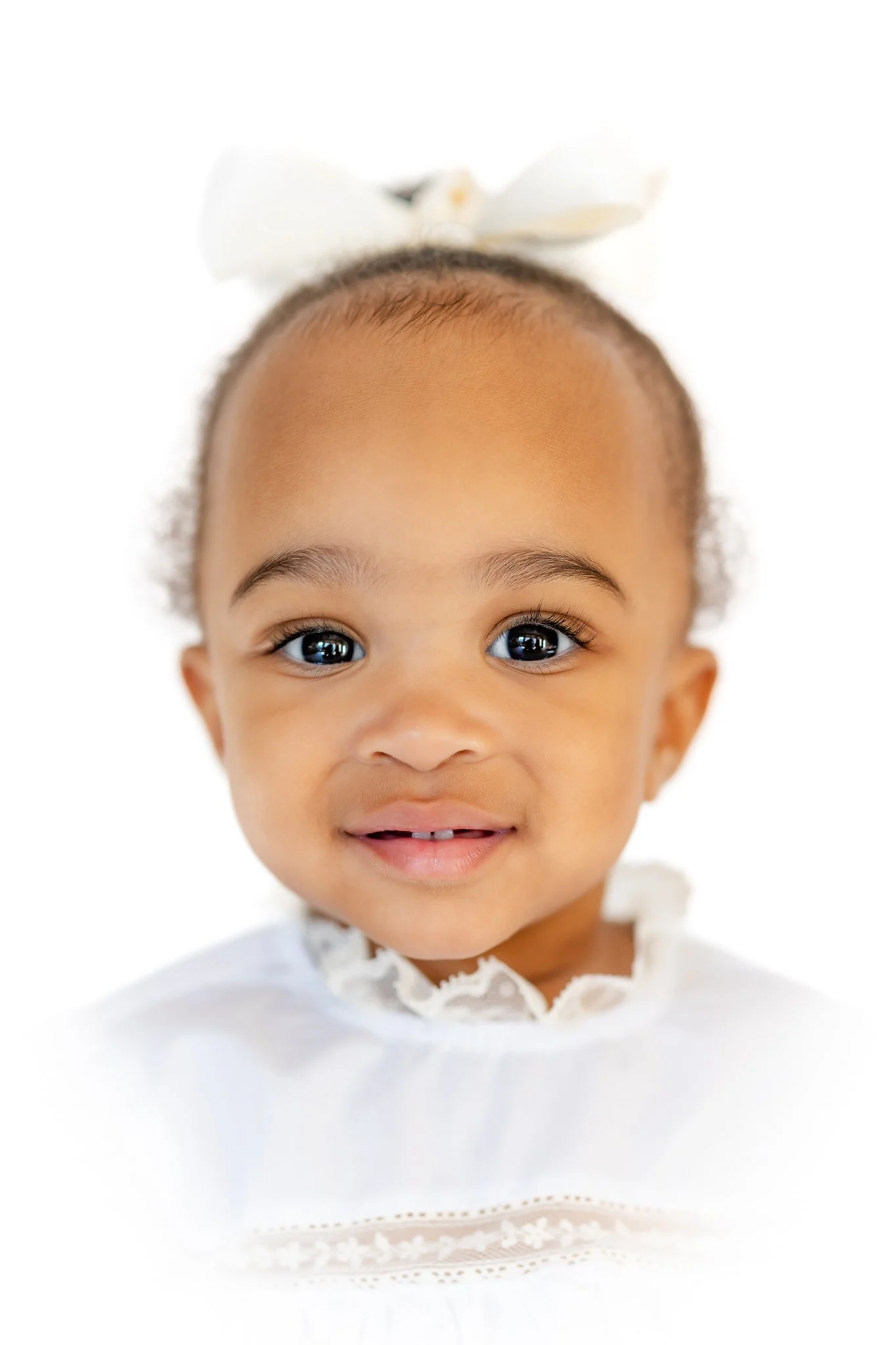 Portrait of a smiling baby with a white bow and lace dress.