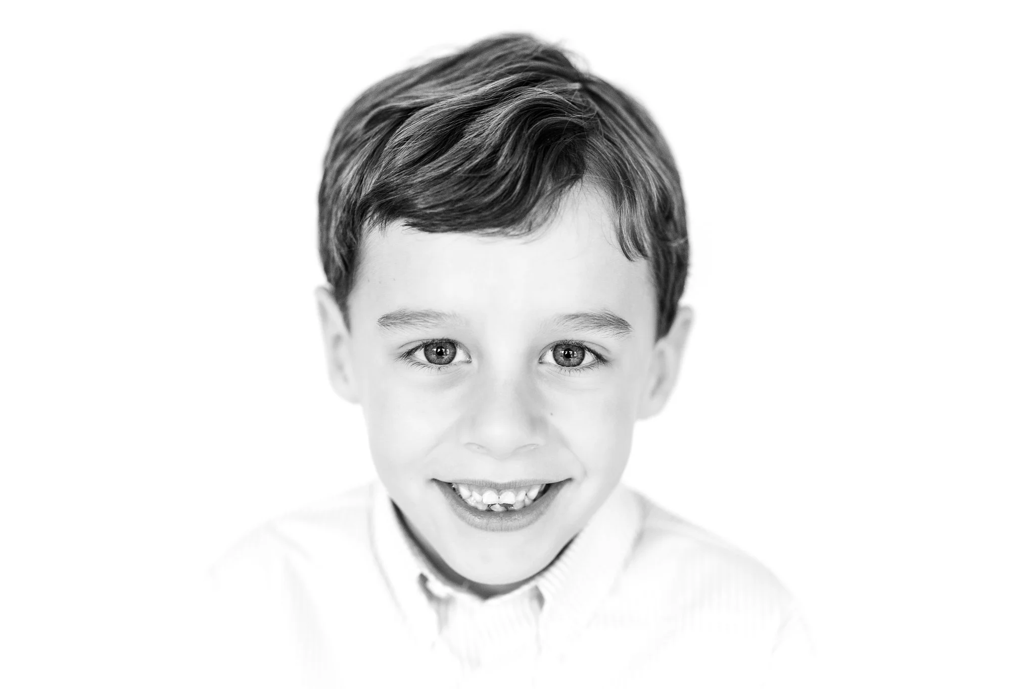 Close-up of a smiling boy in black and white, wearing a light-colored shirt.