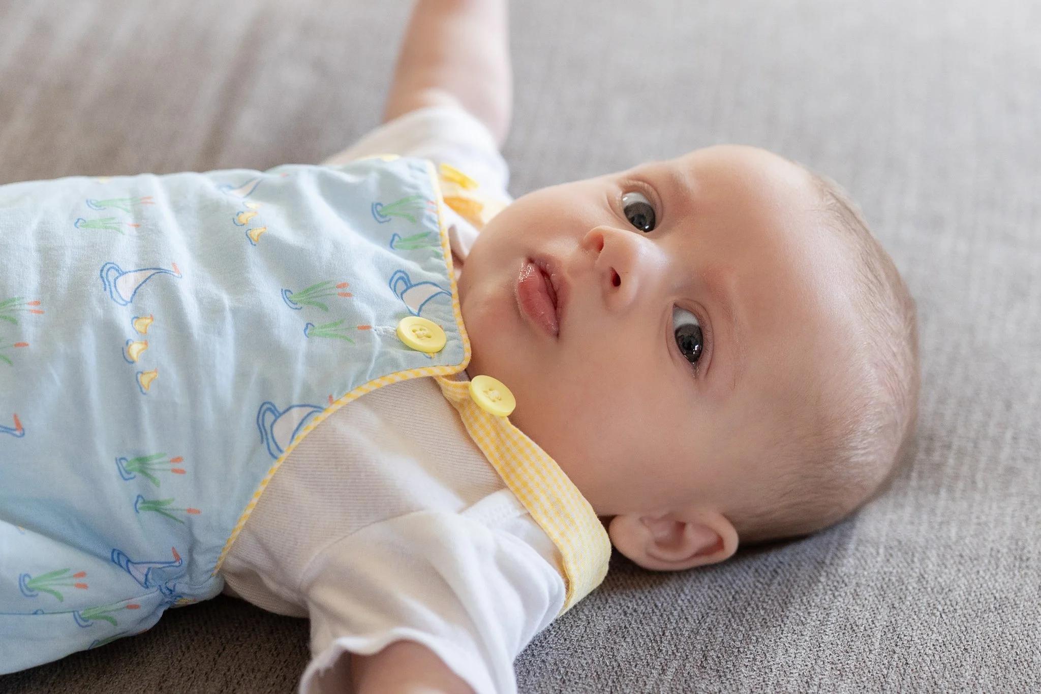 Baby lying on gray fabric wearing a light blue outfit with button details.