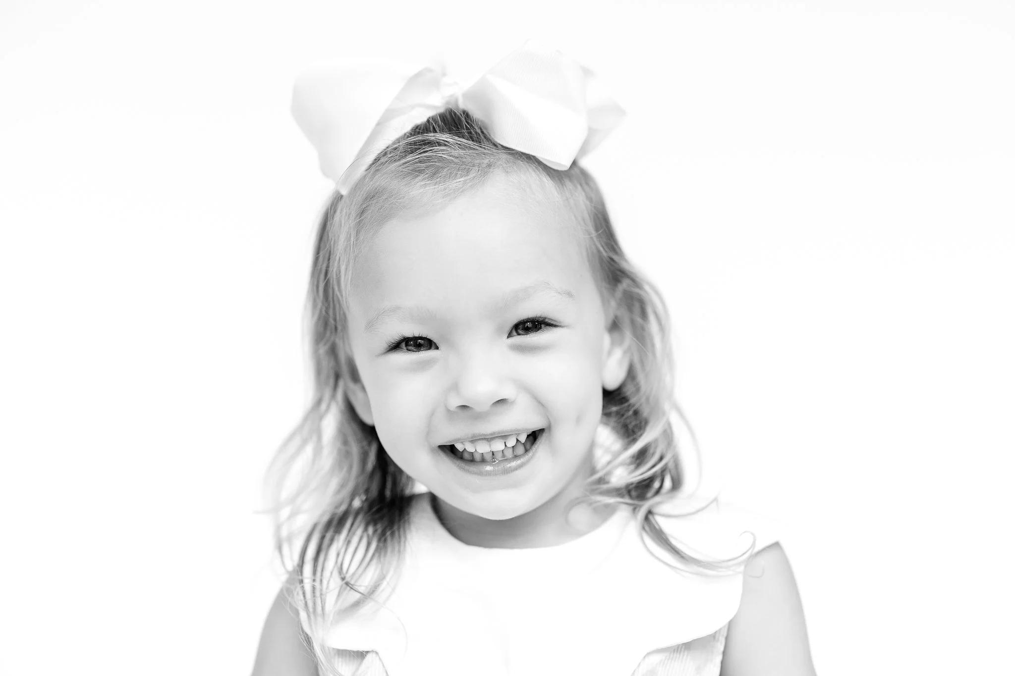 Black and white photo of a smiling child with long hair and a large bow.