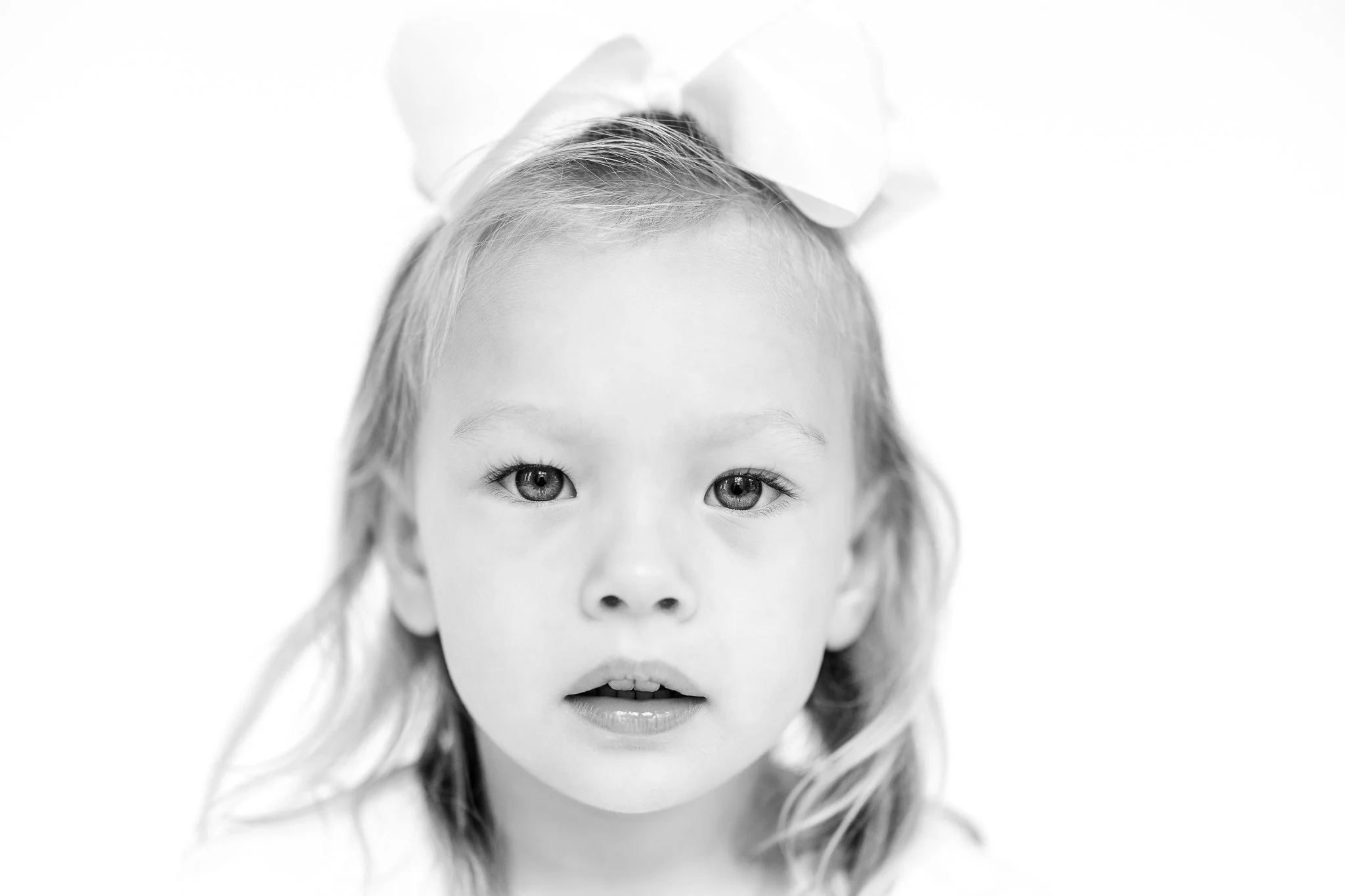 Black and white portrait of a child with a bow in their hair.