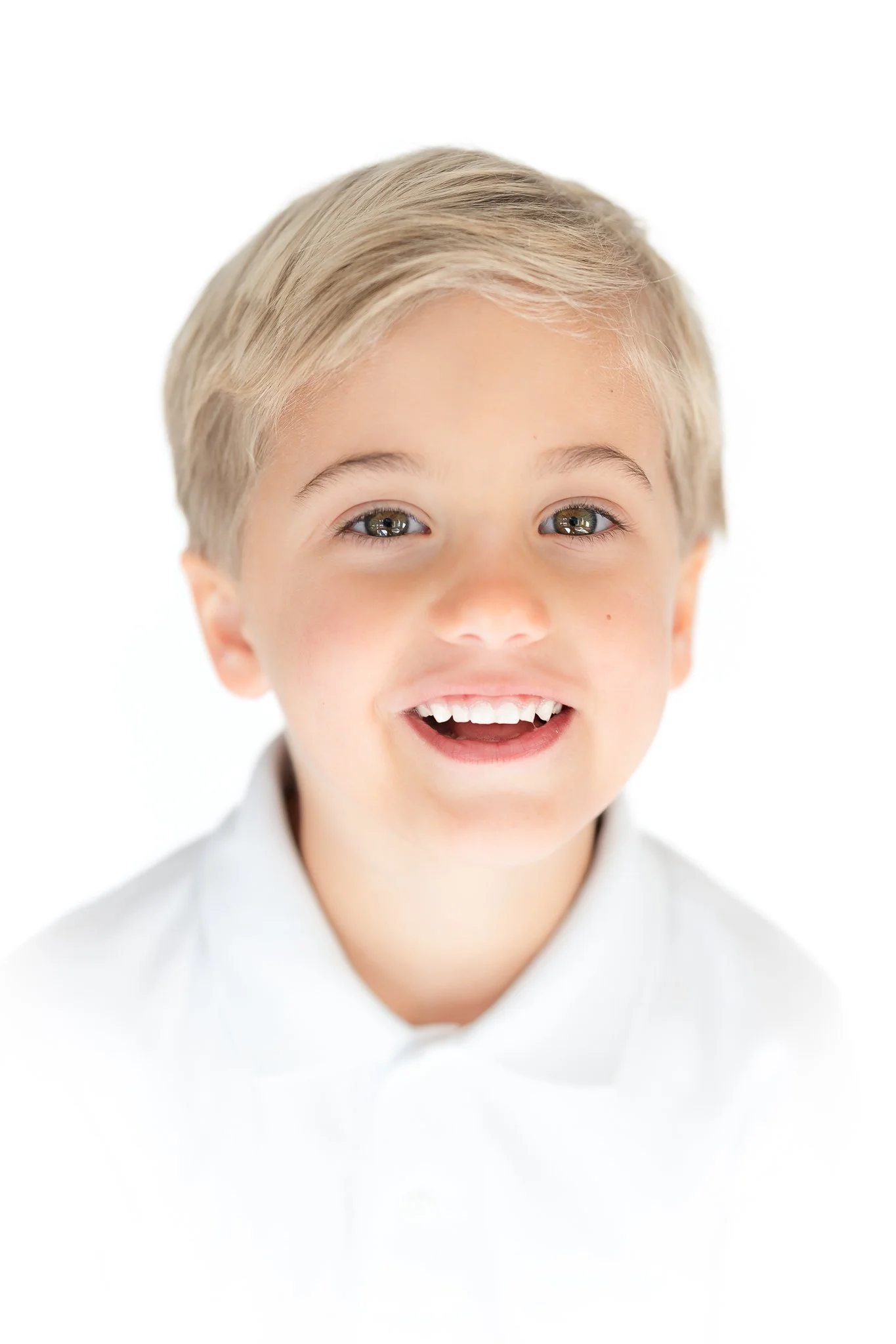 Smiling child with short blonde hair and wearing a white shirt.