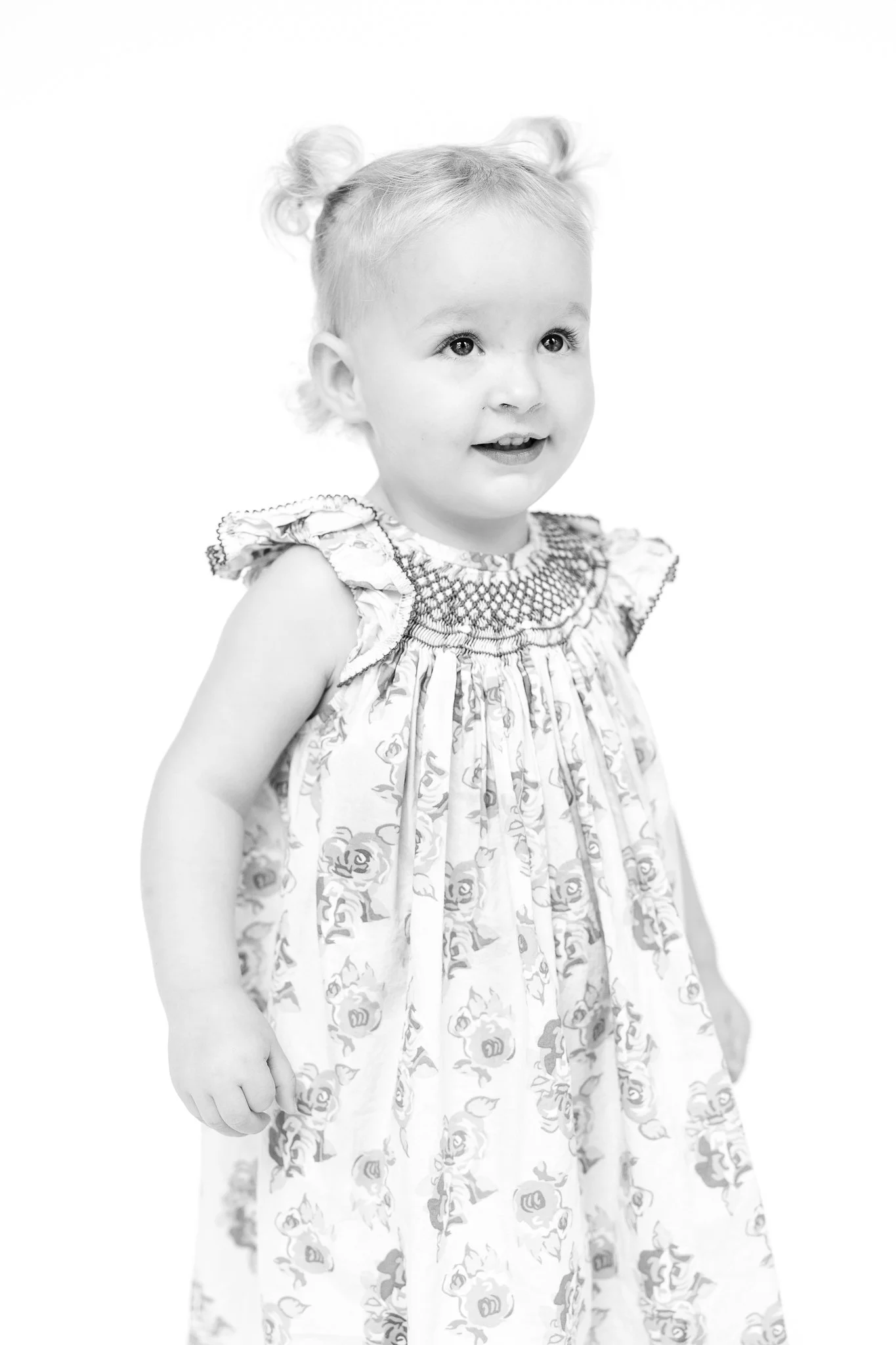 Black and white photo of a young child with light hair in pigtails, wearing a patterned dress with ruffled sleeves, looking to the right.