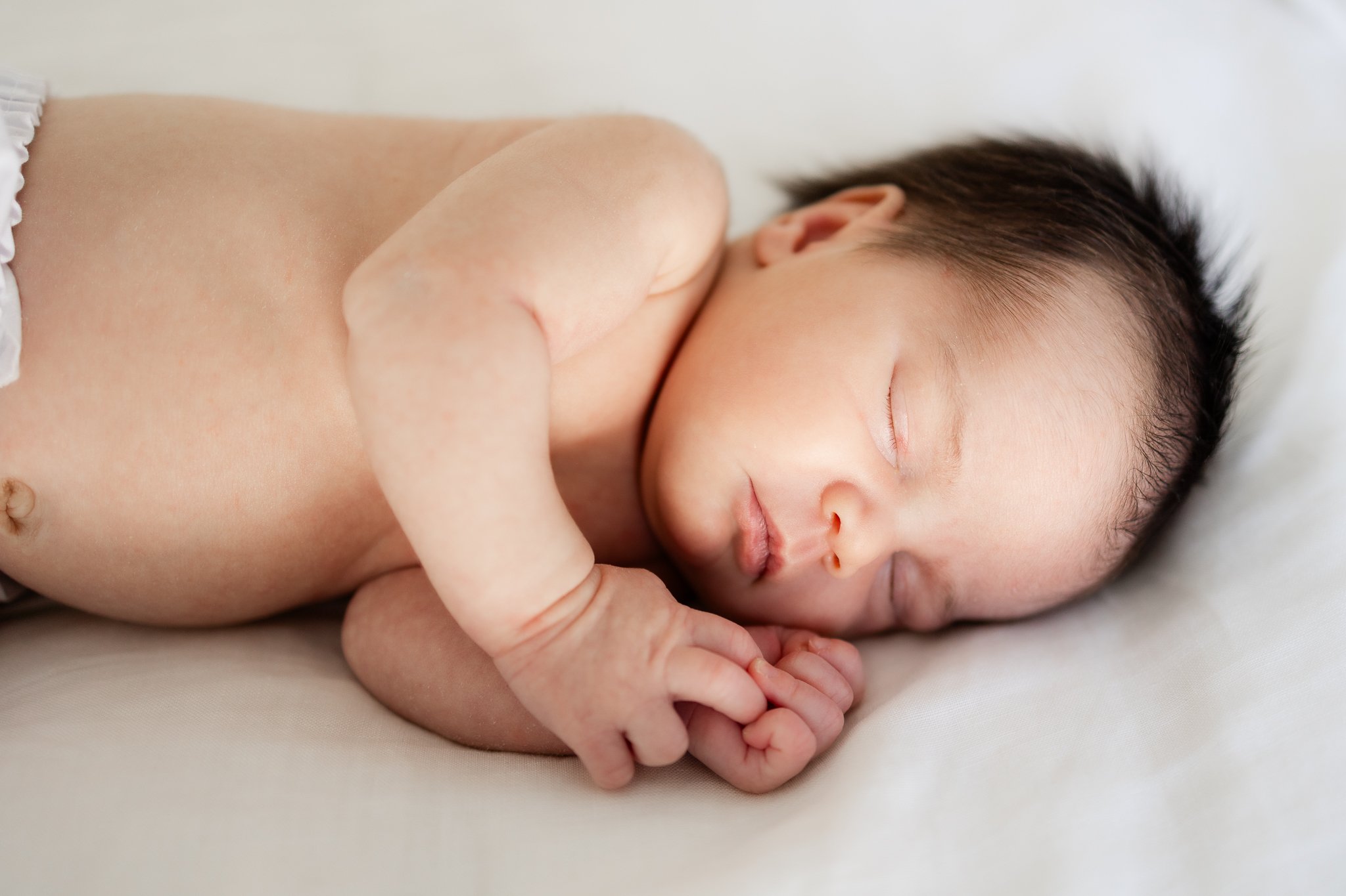Sleeping newborn baby with dark hair lying on white blanket.
