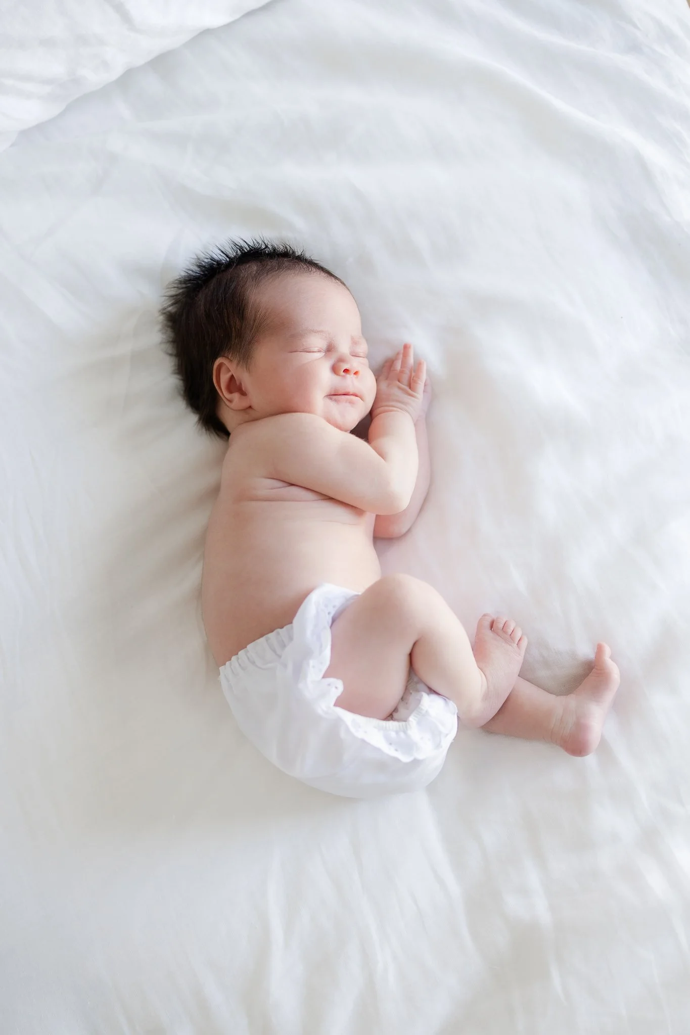 A newborn baby sleeping on a white bed, wearing a diaper.