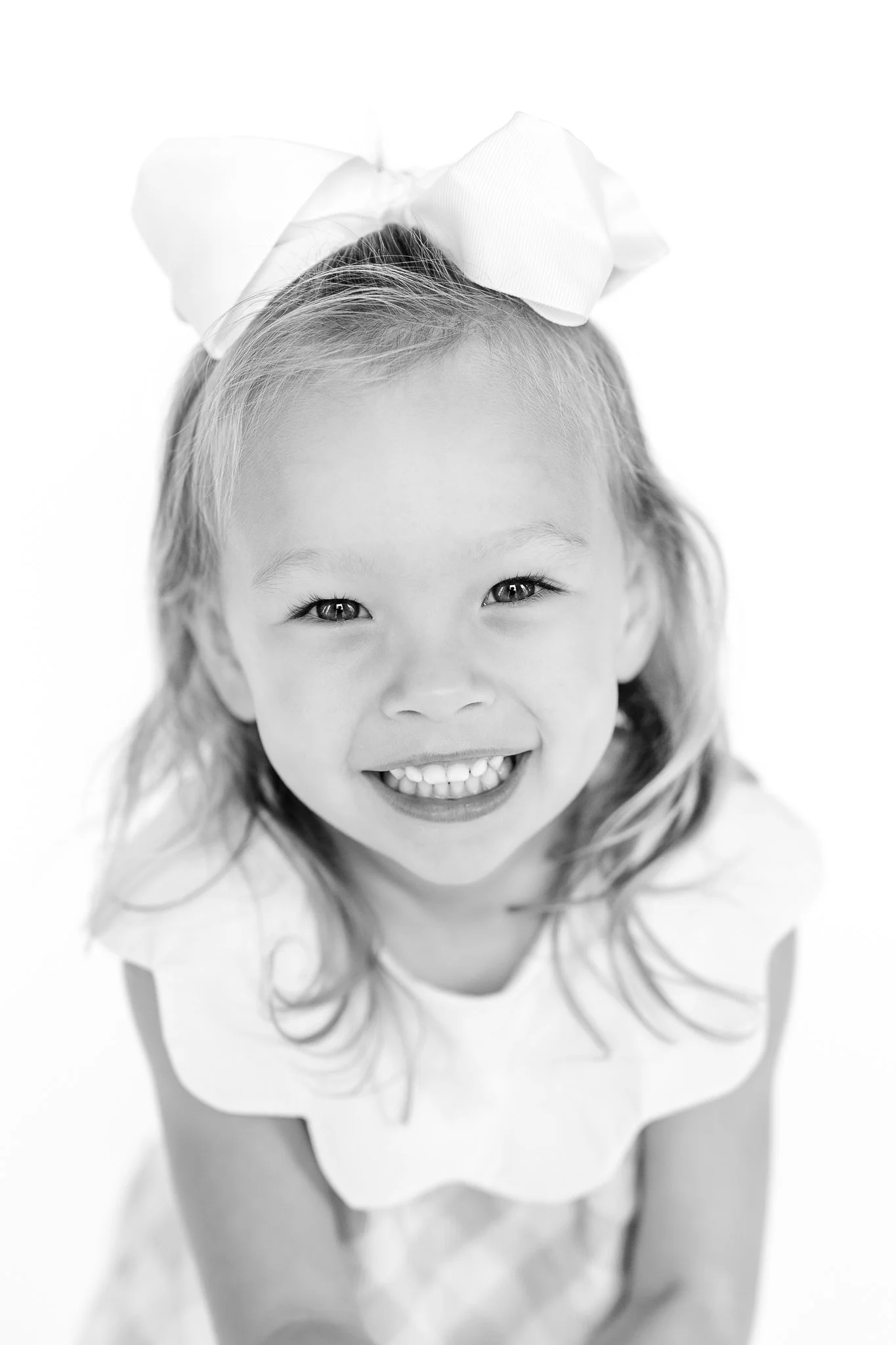 Black and white photo of a smiling little girl with a big bow in her hair.