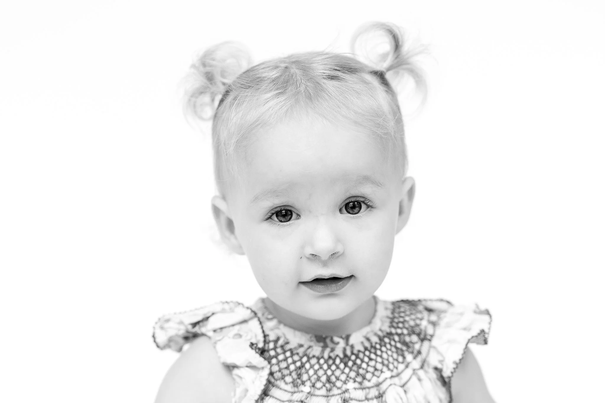 Black and white portrait of a young child with two small ponytails, wearing a patterned top.