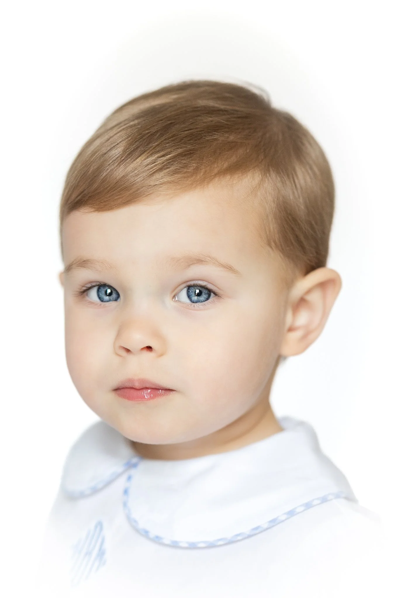 Portrait of a young child with short brown hair and blue eyes, wearing a white outfit.
