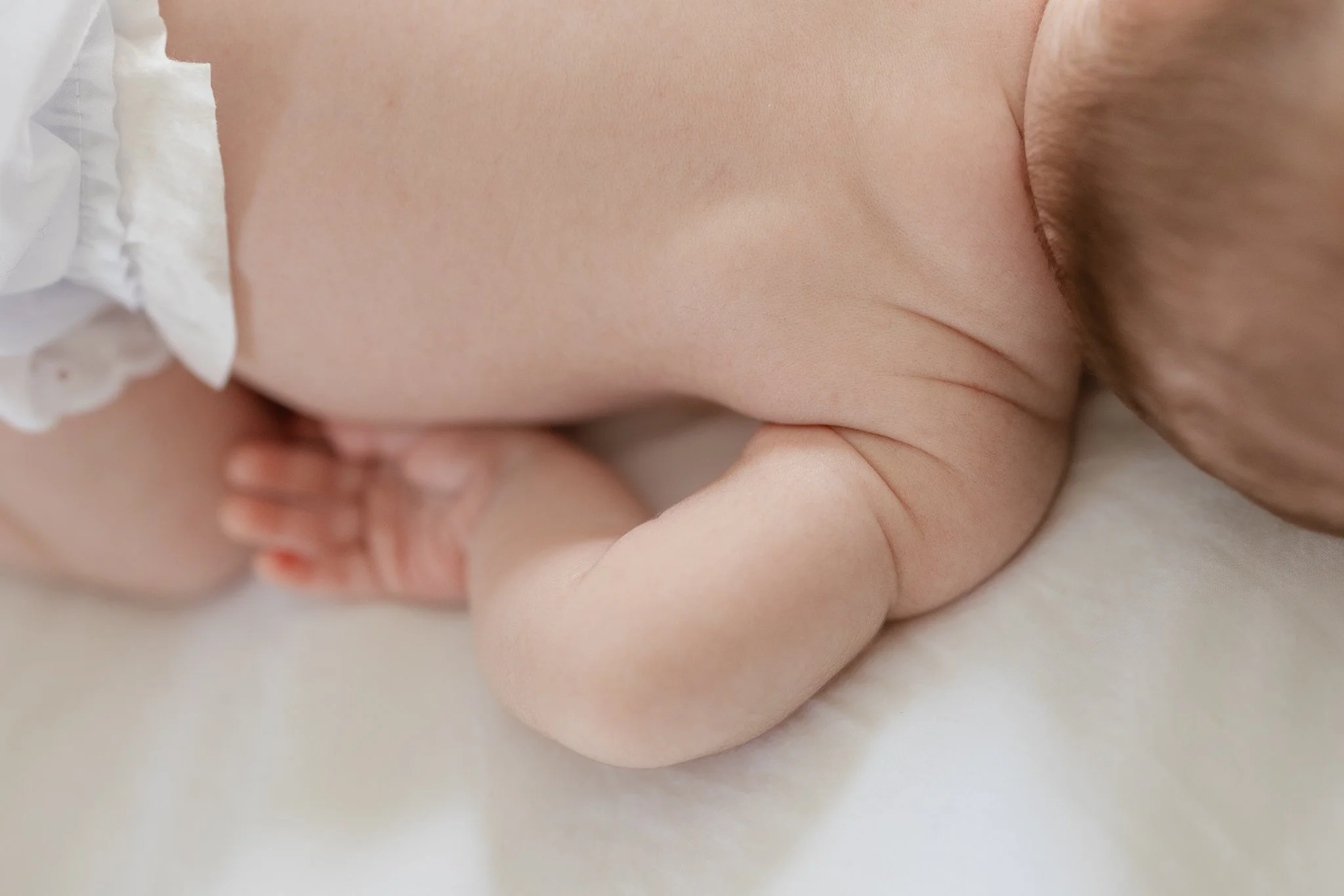Close-up of a baby lying on a white blanket, showing the back and arm.