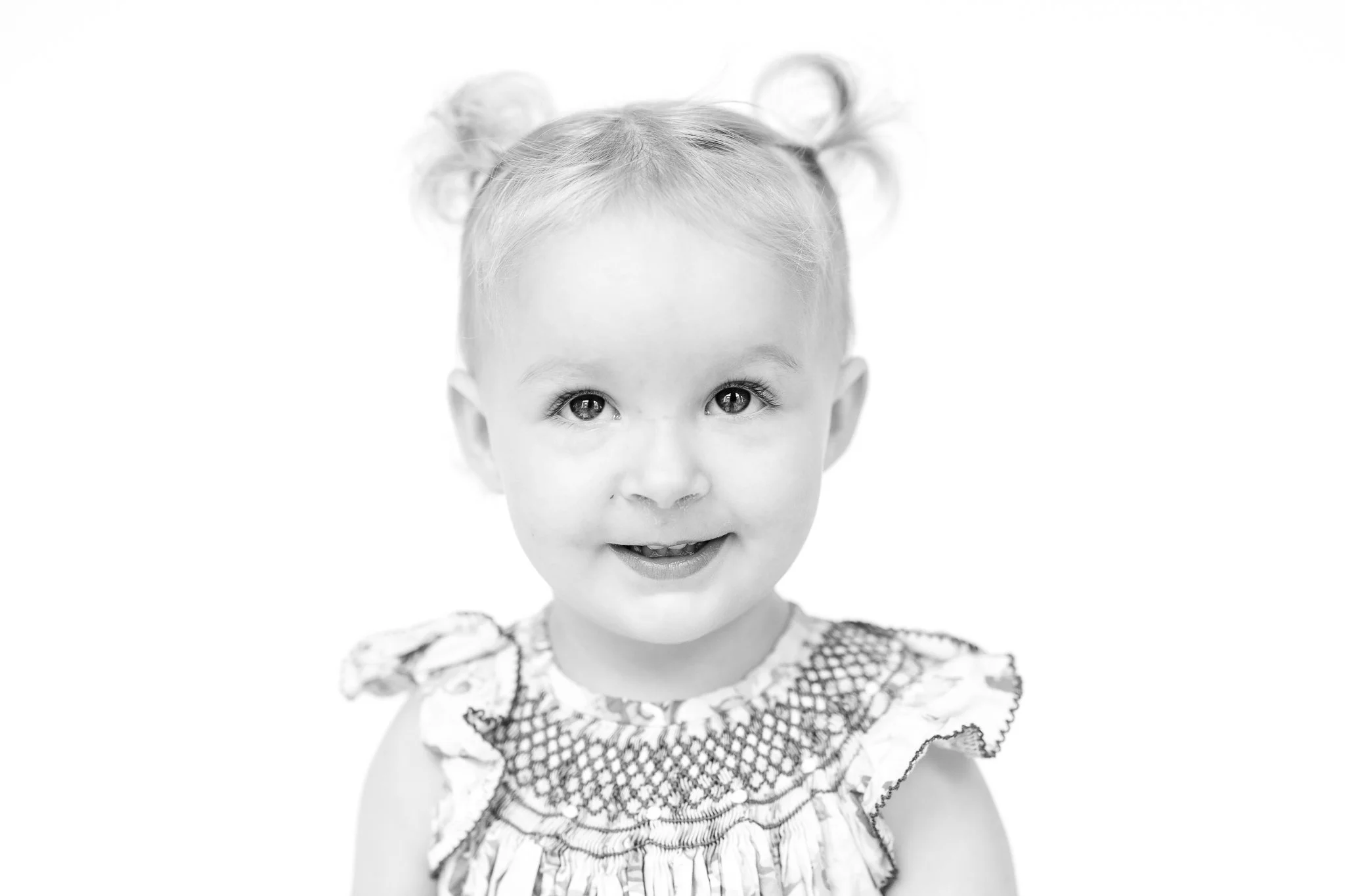 Black and white portrait of a smiling toddler with pigtails.