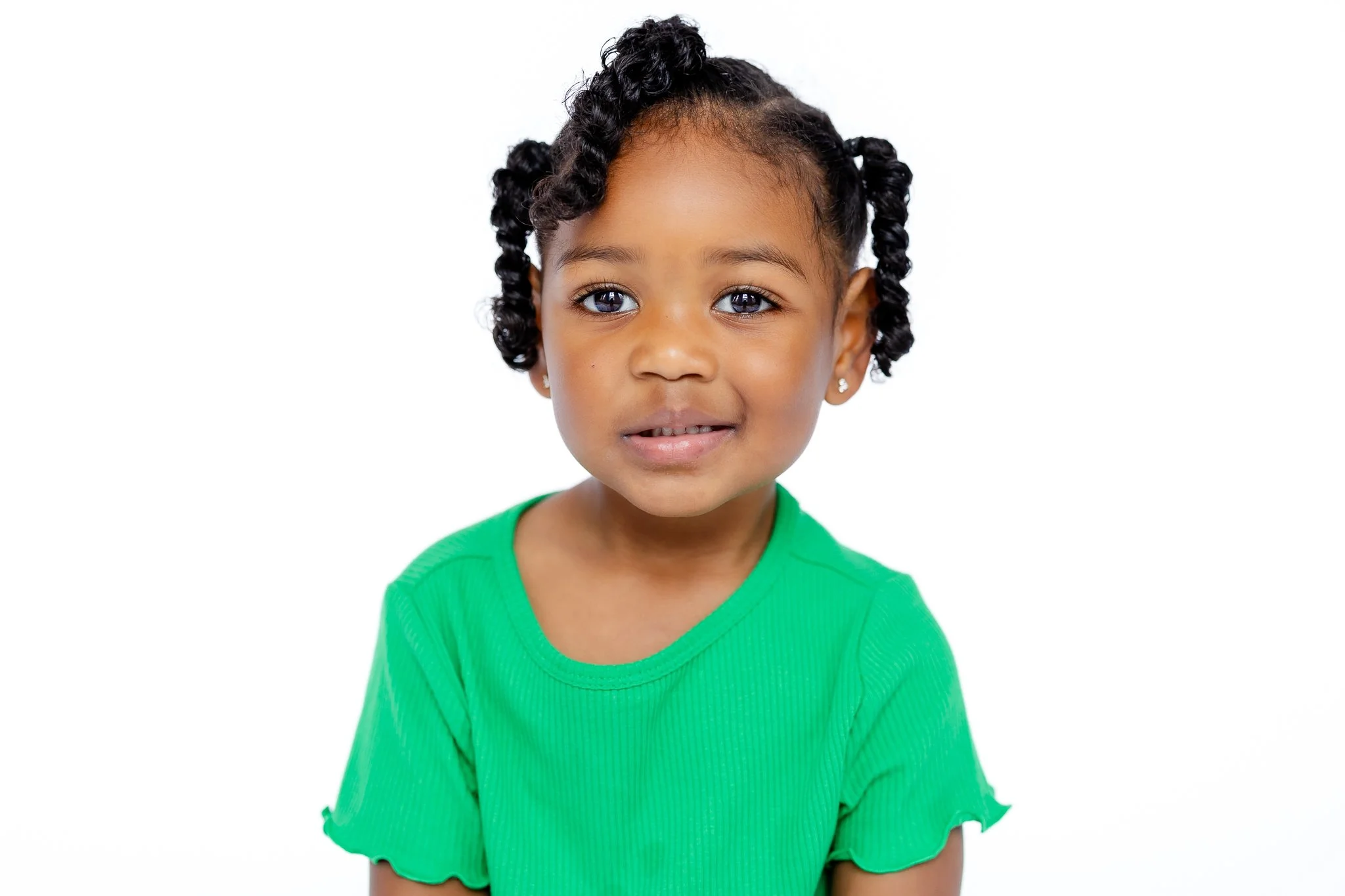 Young child in a green shirt smiling against a white background.