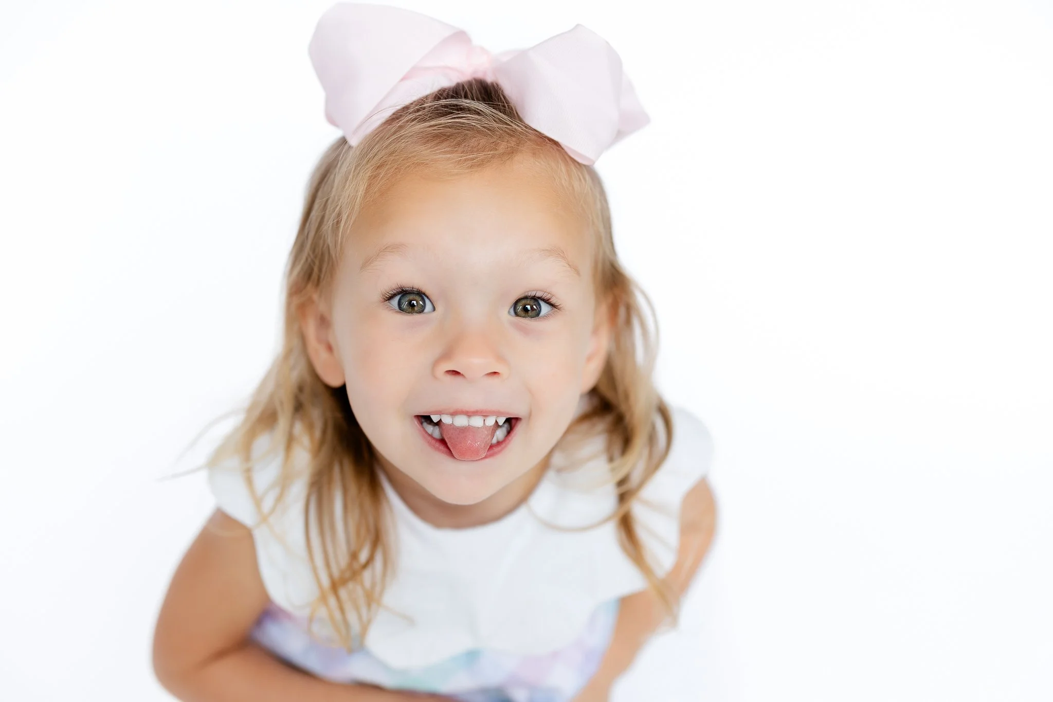 Young girl with a pink bow sticking out her tongue playfully.
