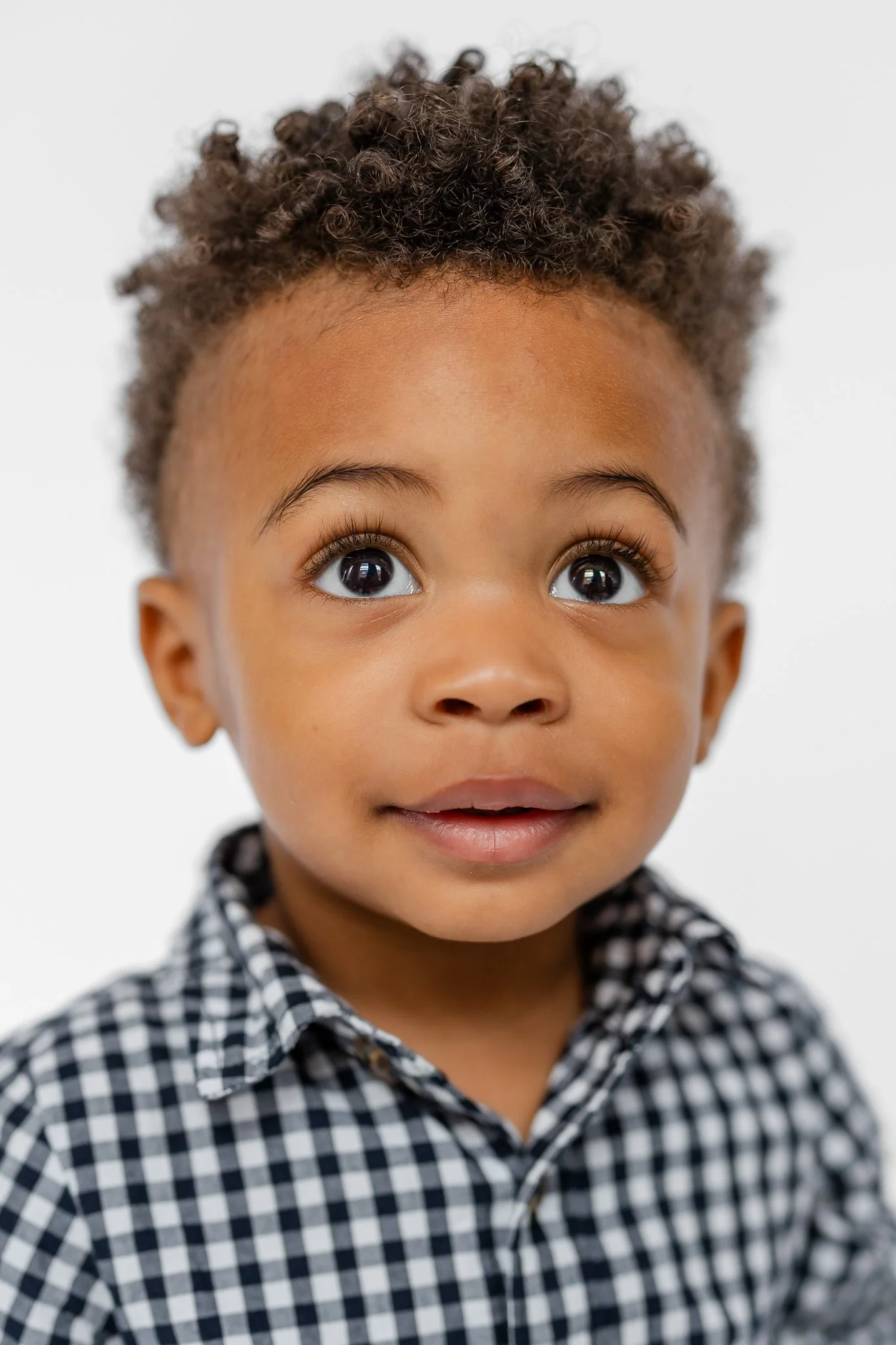 Young child with curly hair, wearing a black and white checkered shirt, looking upwards.