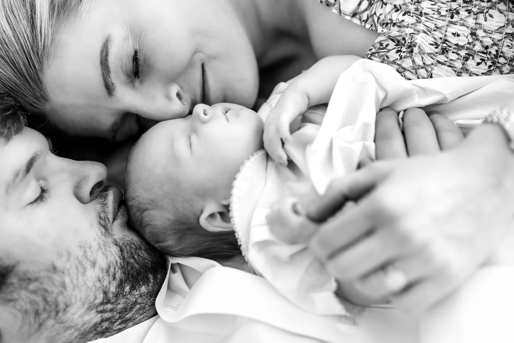 Black and white photo of a couple lovingly embracing their sleeping newborn baby.