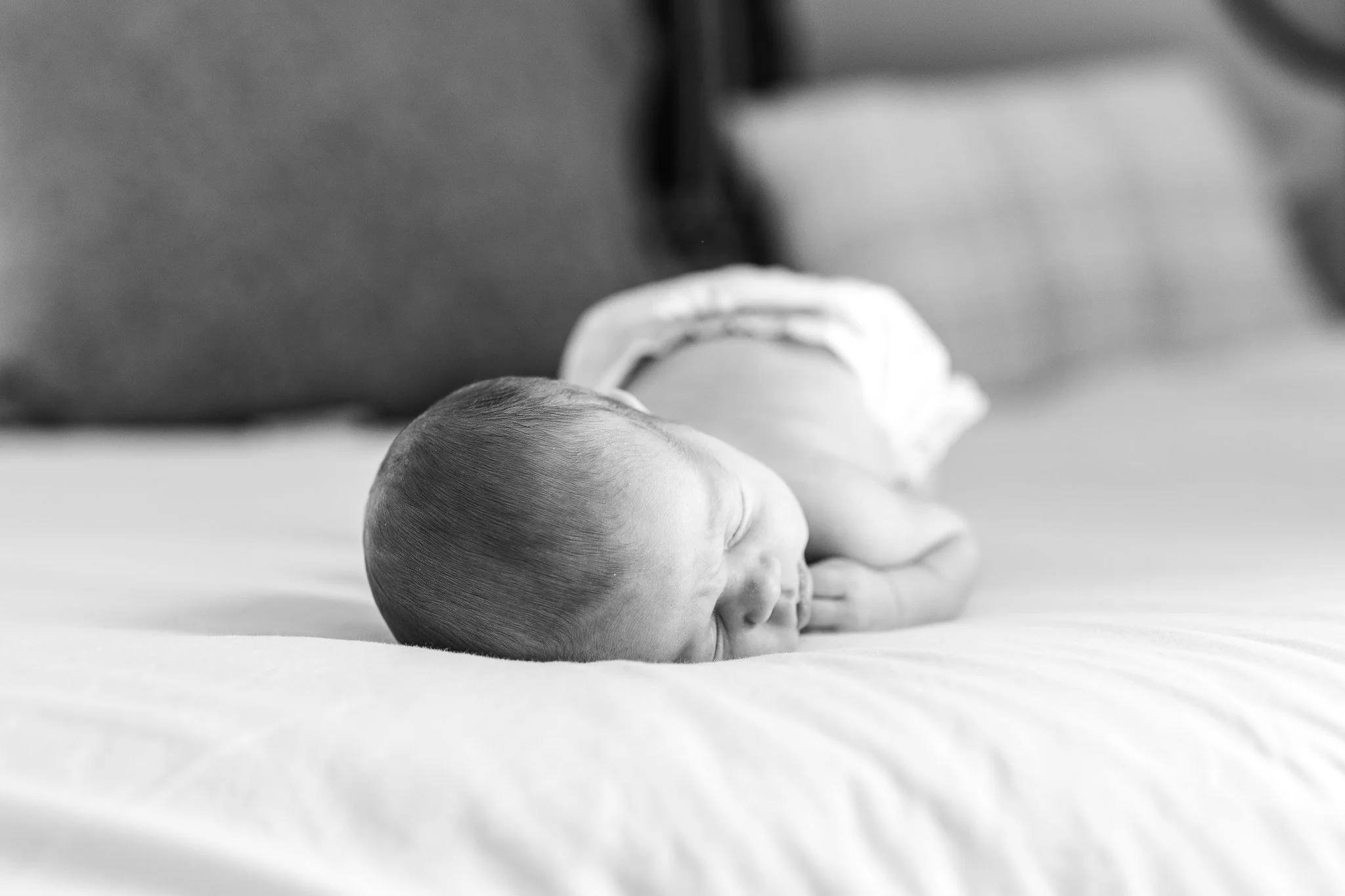 Black and white photo of a newborn baby sleeping on a bed.