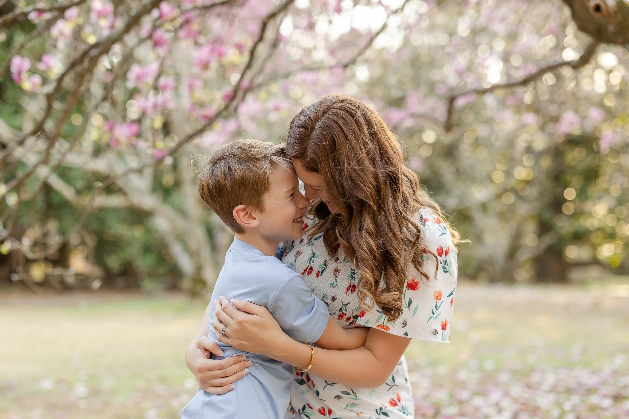 A woman hugging a boy in a park with blooming trees.