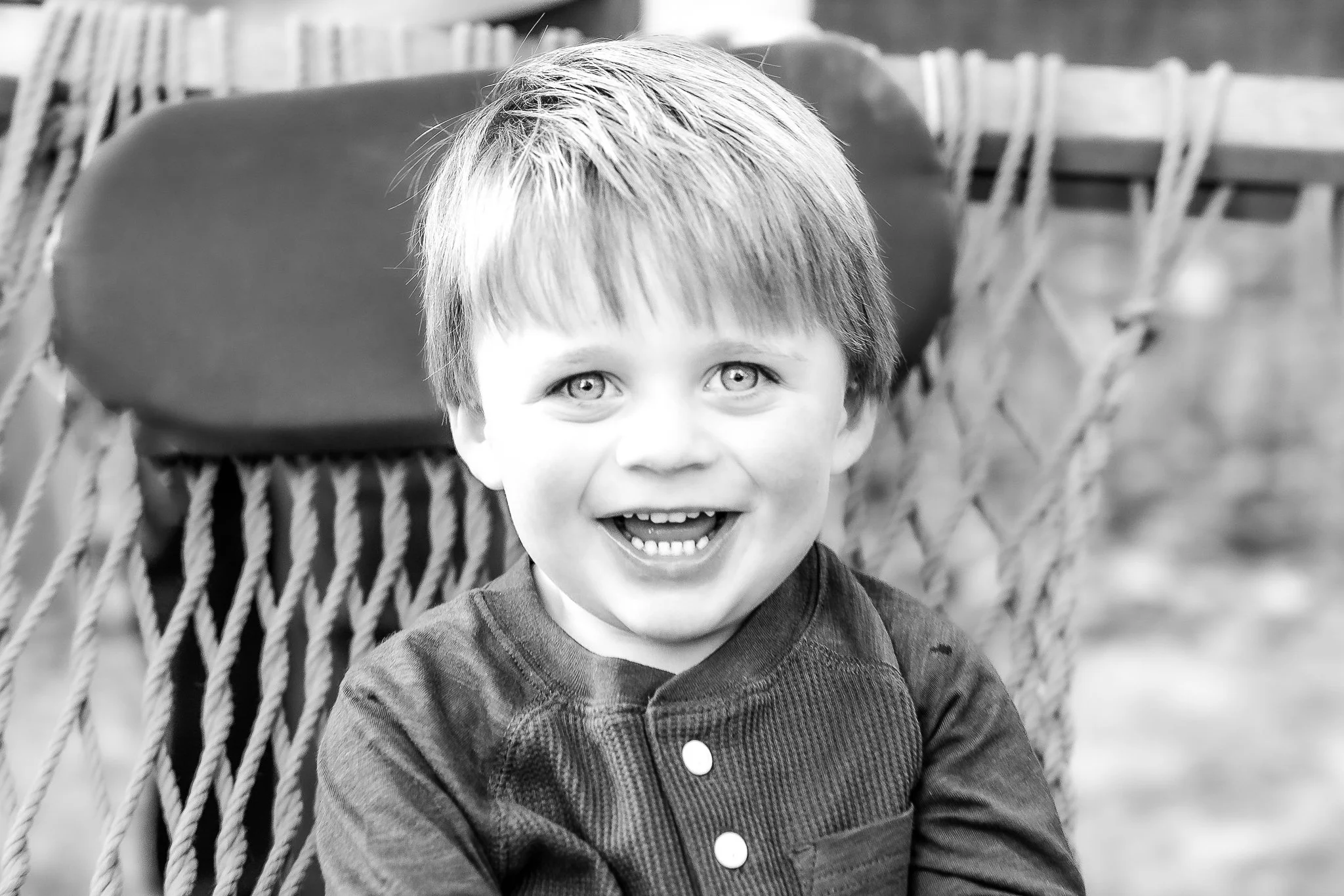 Black and white photo of a smiling child sitting on a hammock.