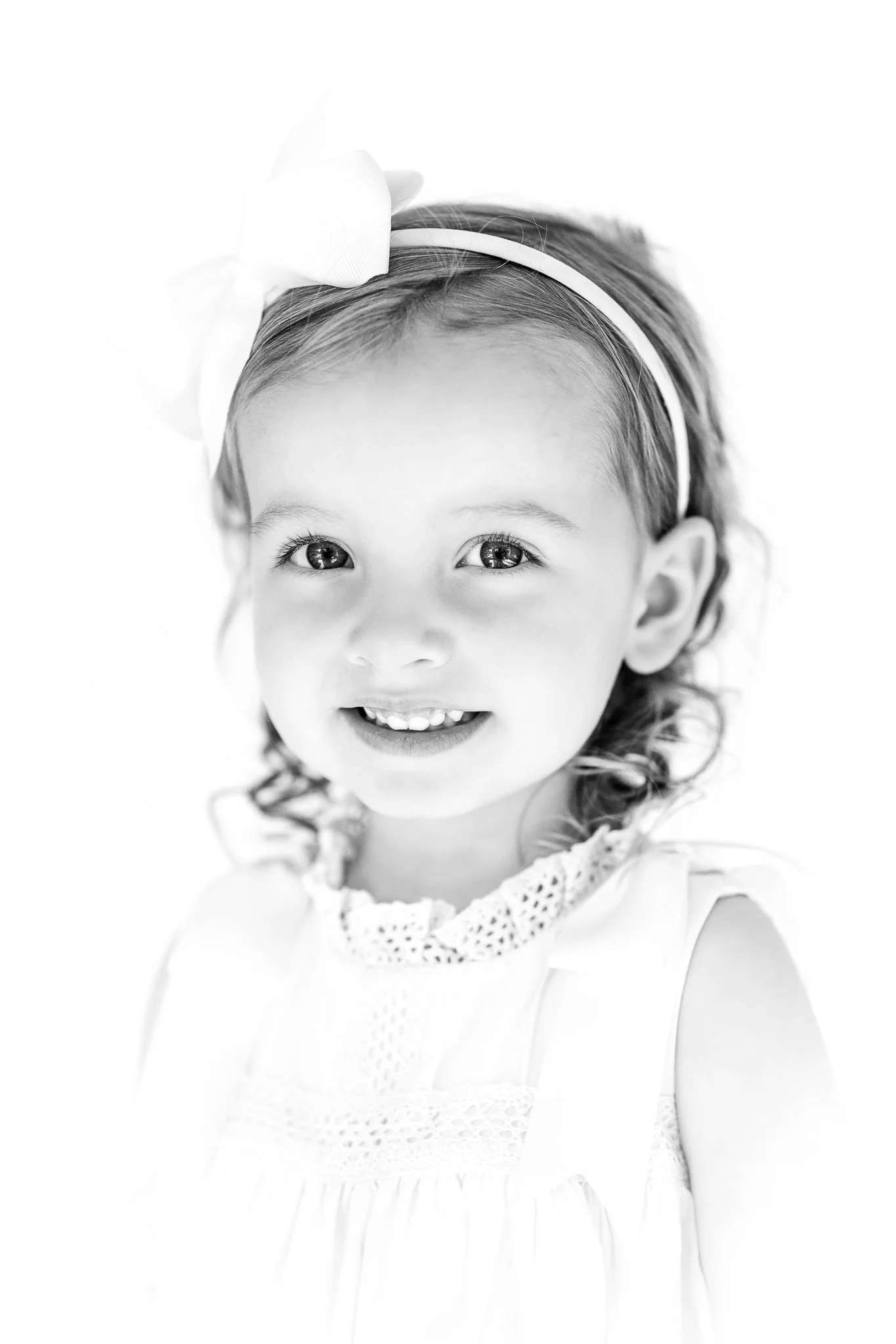 Black and white portrait of a young girl wearing a headband with a bow, smiling.