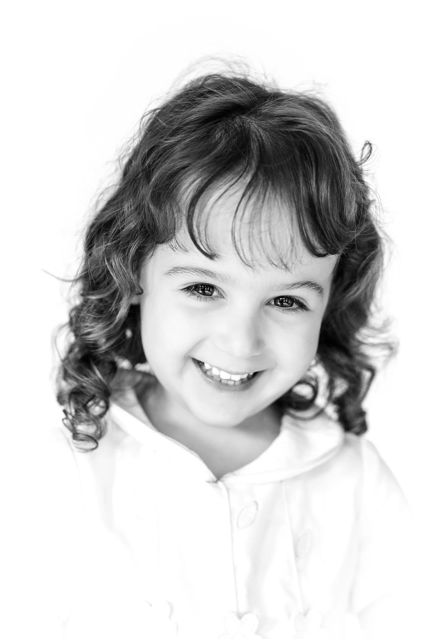 Black and white portrait of a smiling young child with curly hair.