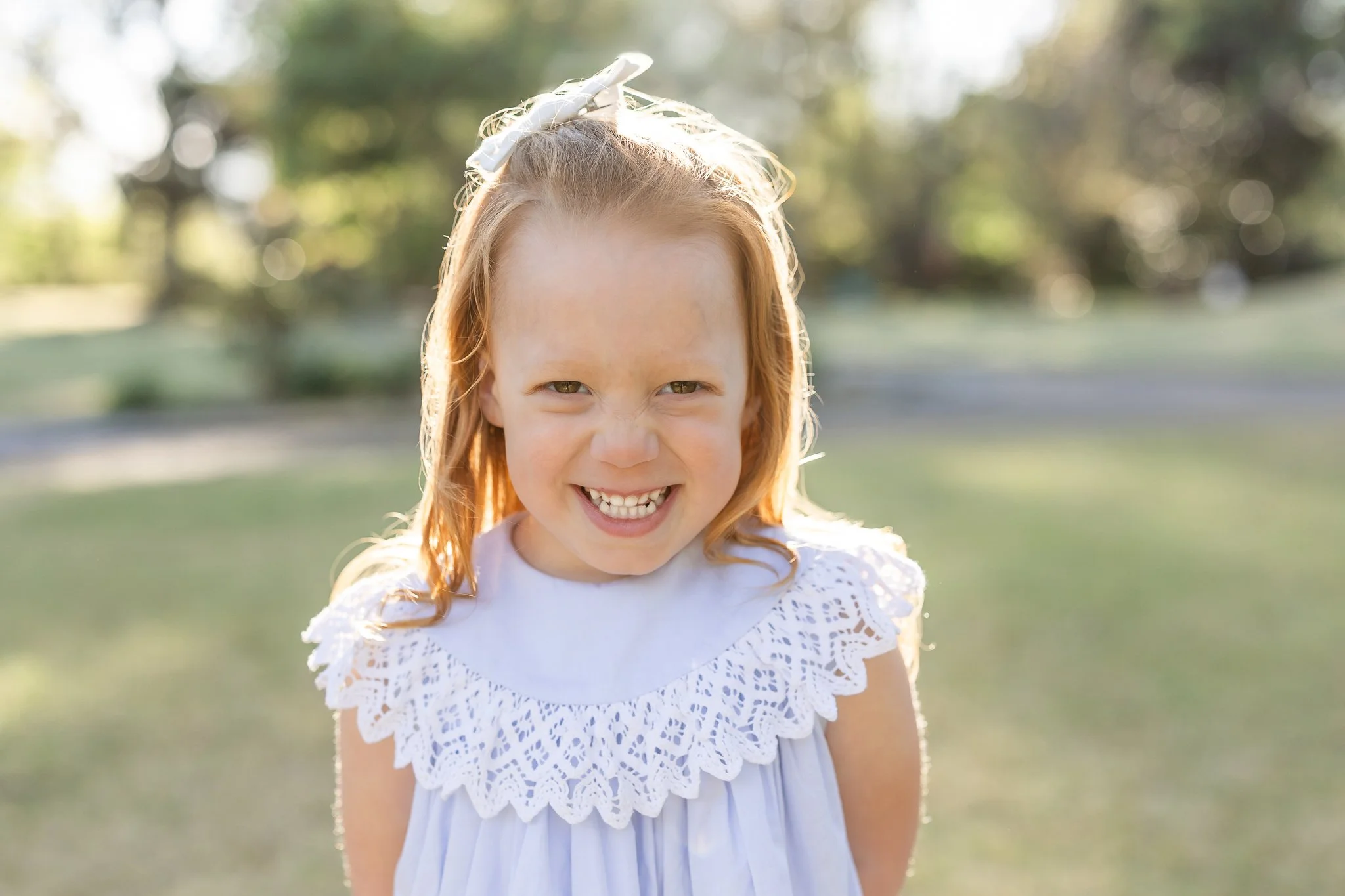 Smiling girl in a white dress with lace collar standing outdoors in a park.