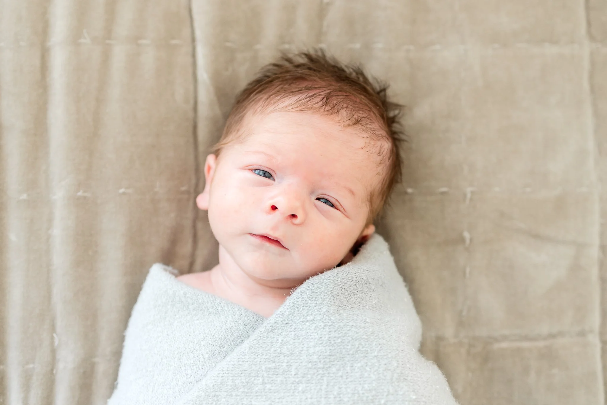 Newborn baby wrapped in a light blanket lying on a soft surface.