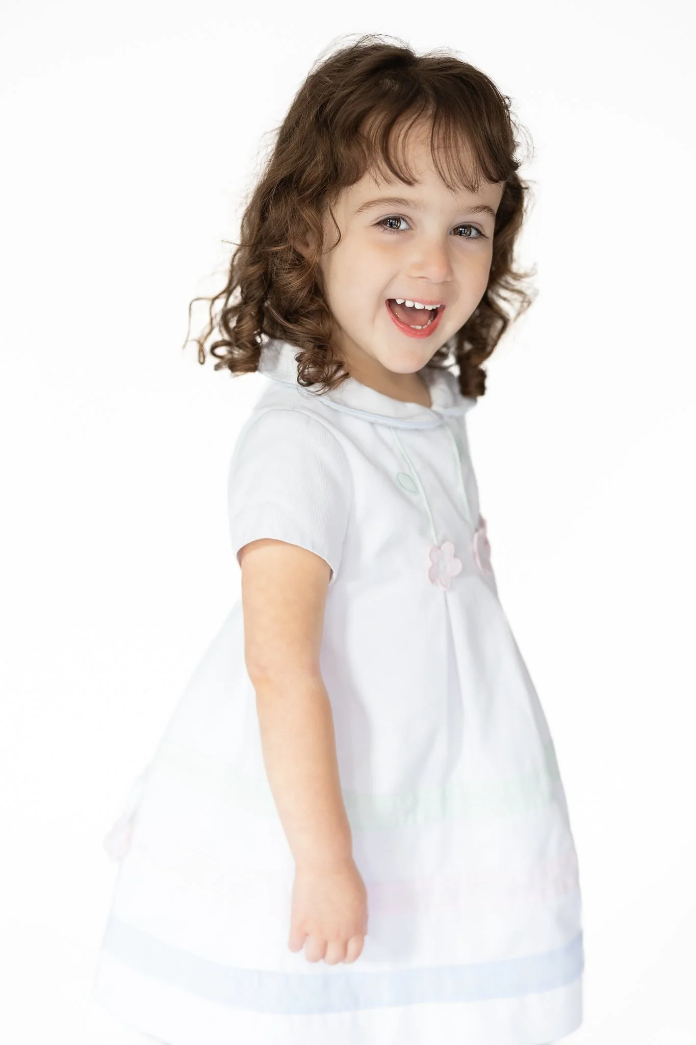 Smiling child in a white dress with curly hair on a white background.