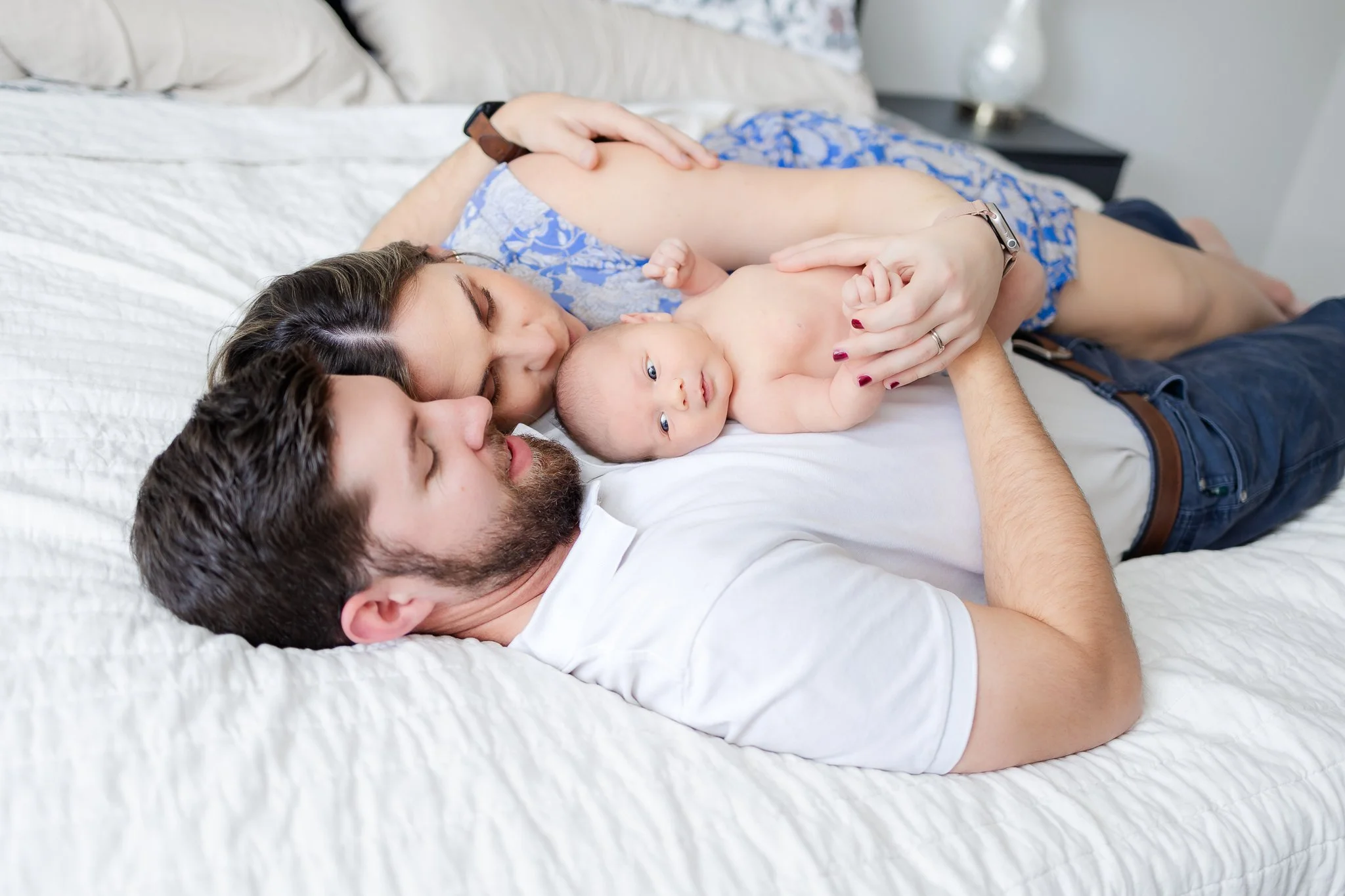 A couple lying on a bed with their newborn baby.