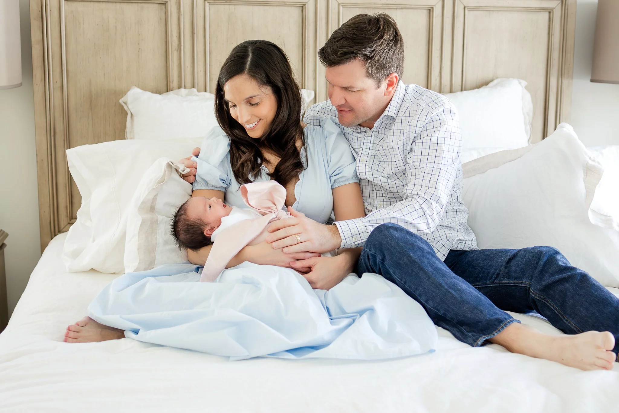 A mother holding a newborn baby, sitting with a father on a bed.