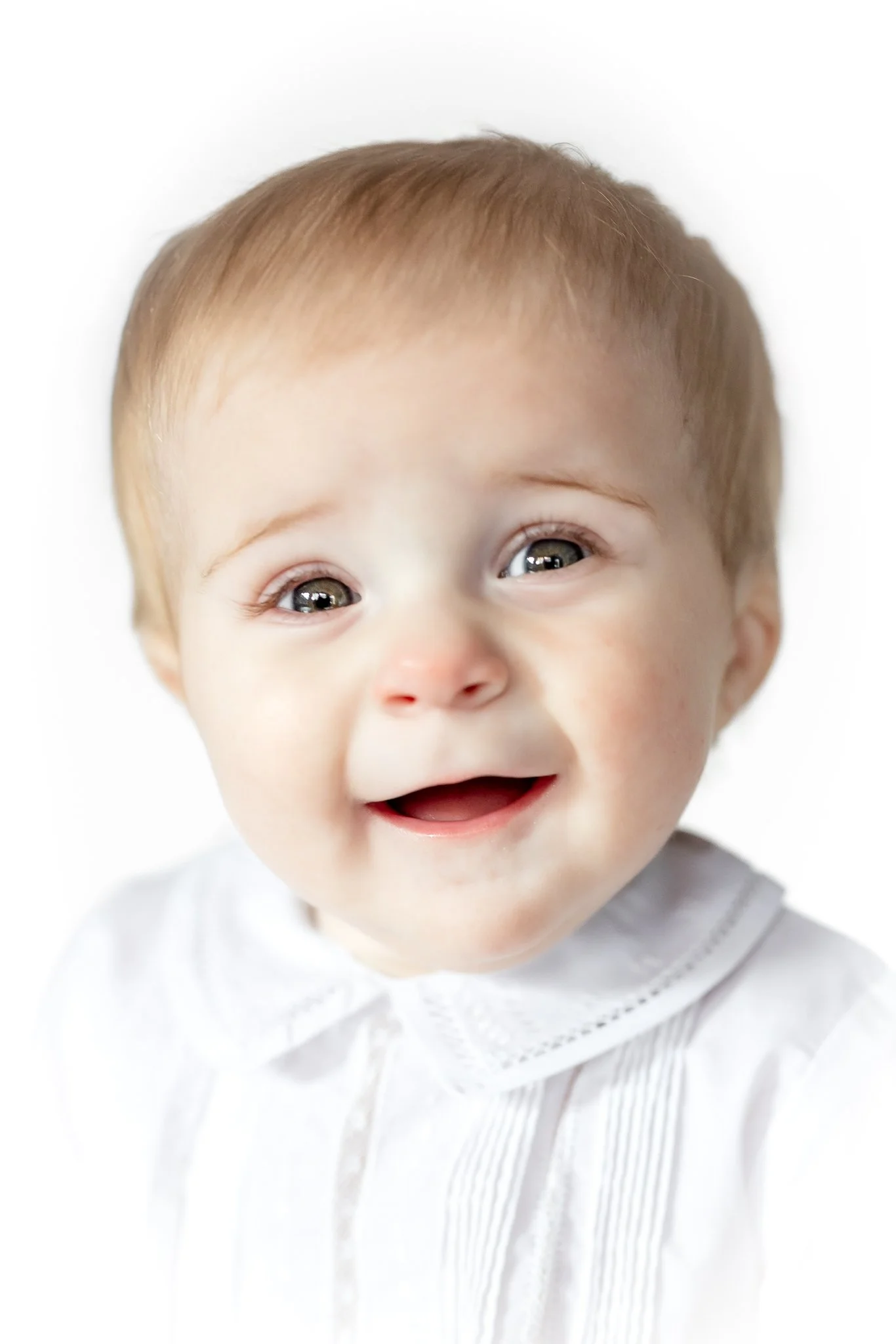 Smiling baby wearing a white outfit with a lace collar.
