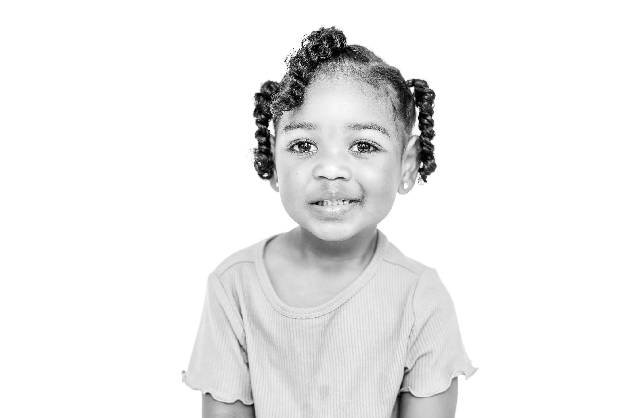 Black and white portrait of a smiling child with curly hair and a ribbed shirt.