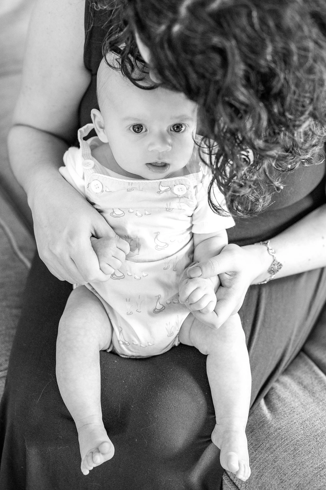 Black and white photo of a baby sitting on an adult's lap, holding hands.