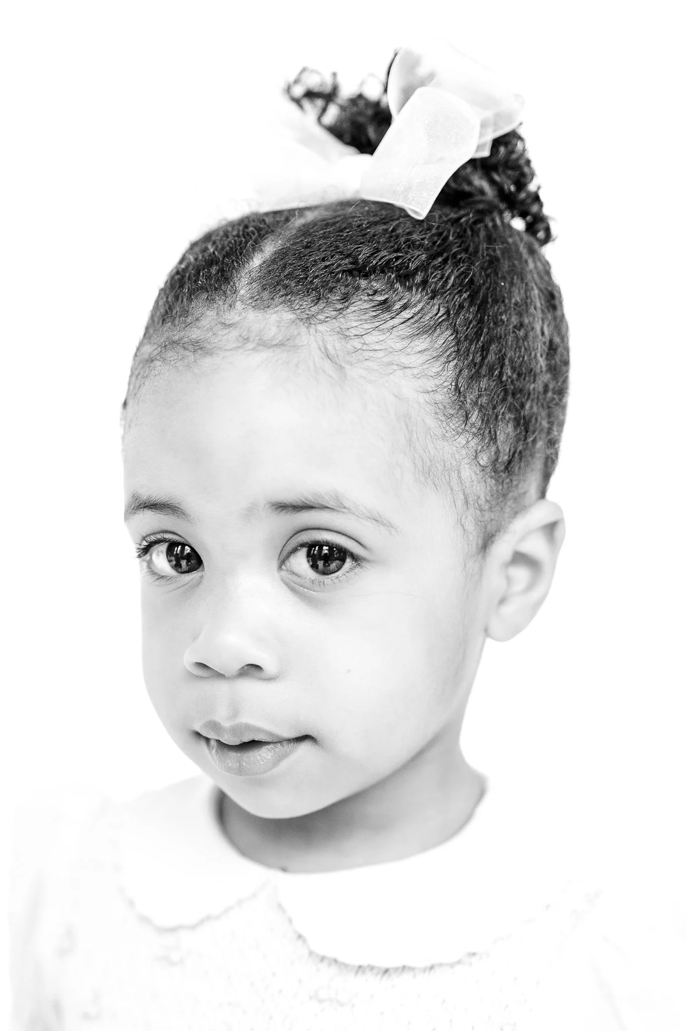 Black and white portrait of a young girl with a bow in her hair, looking slightly to the side.