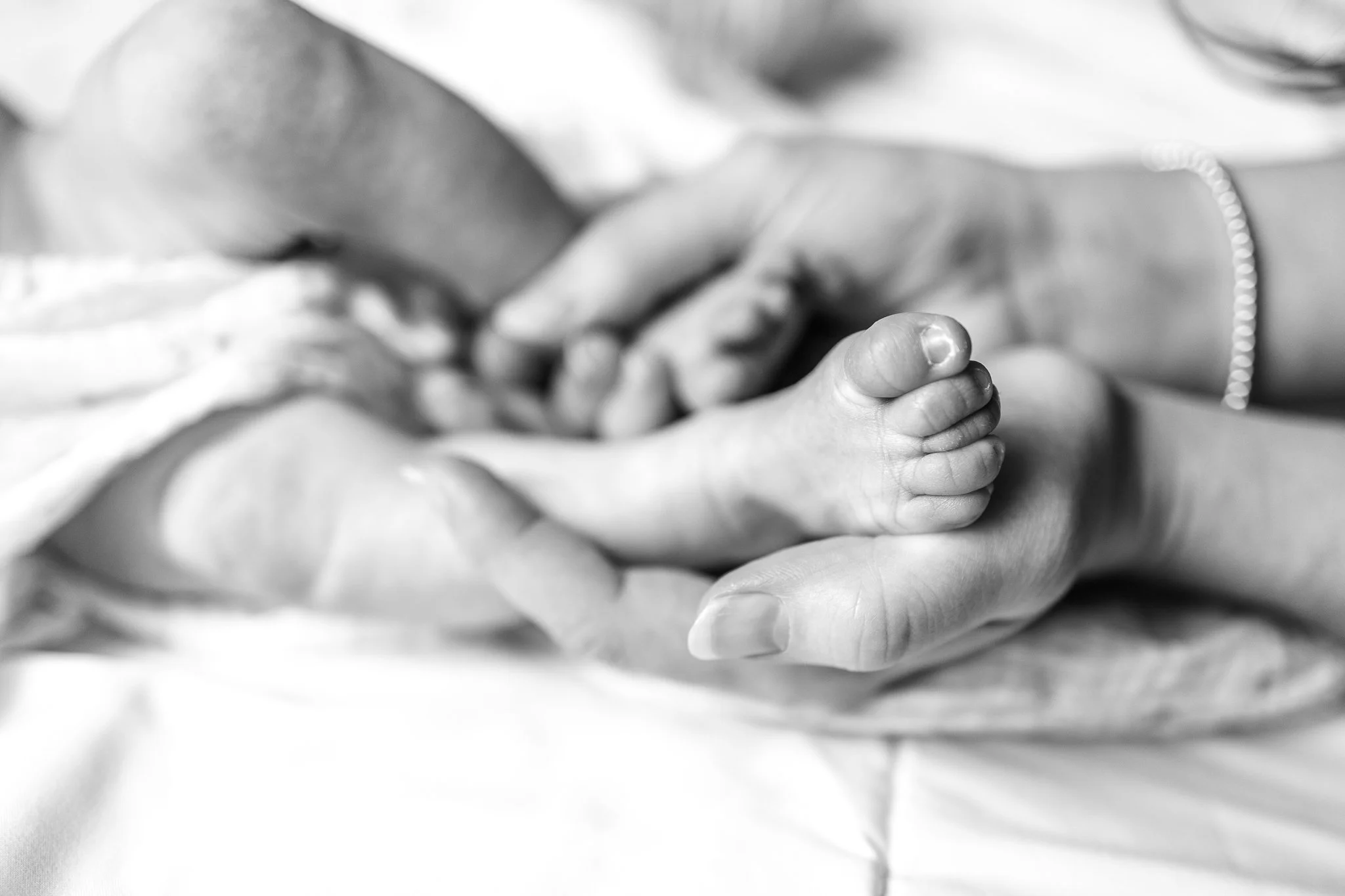 Black and white image of a baby’s feet held gently by an adult's hands.