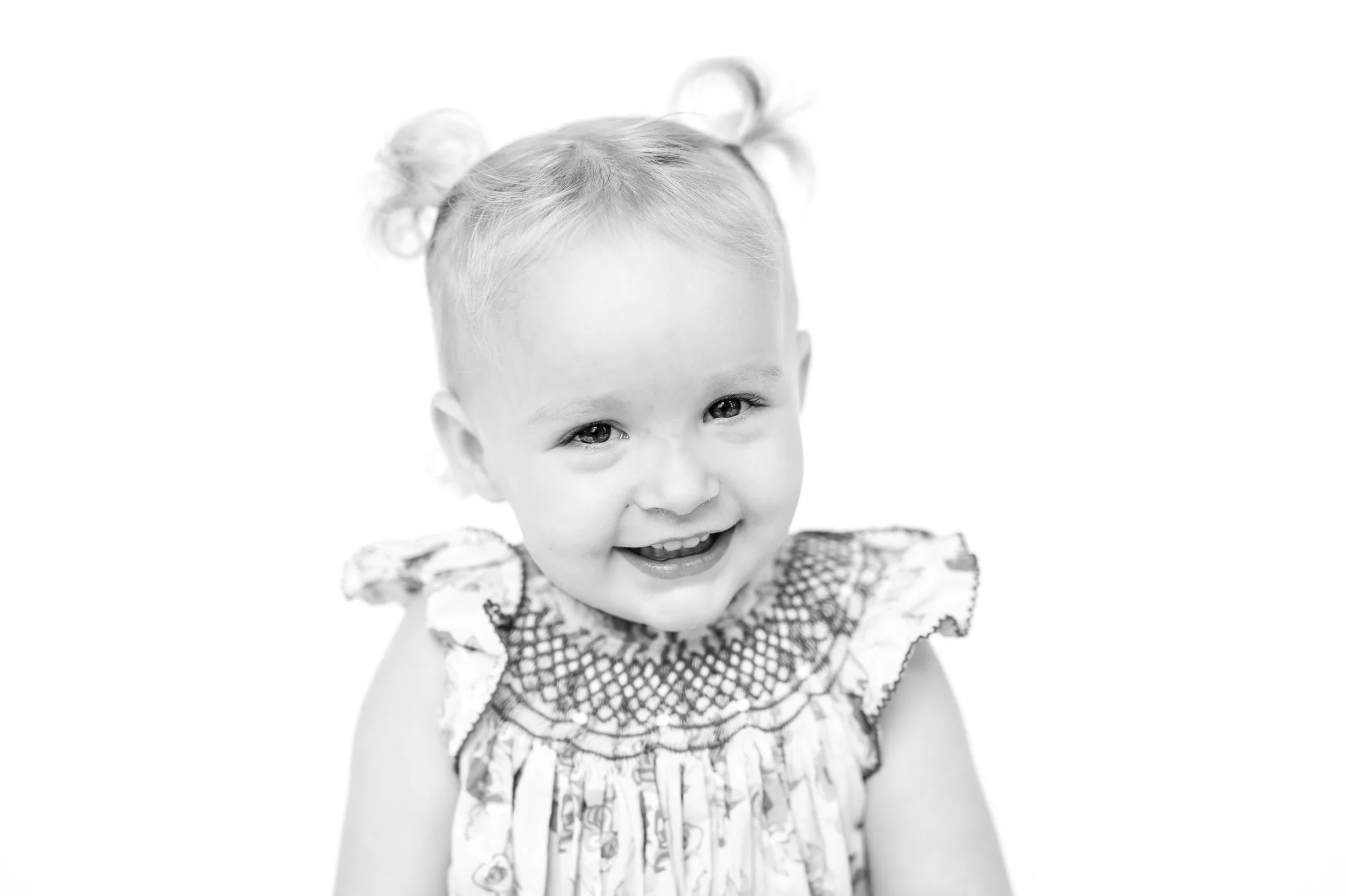 Black and white portrait of a smiling toddler with pigtails.