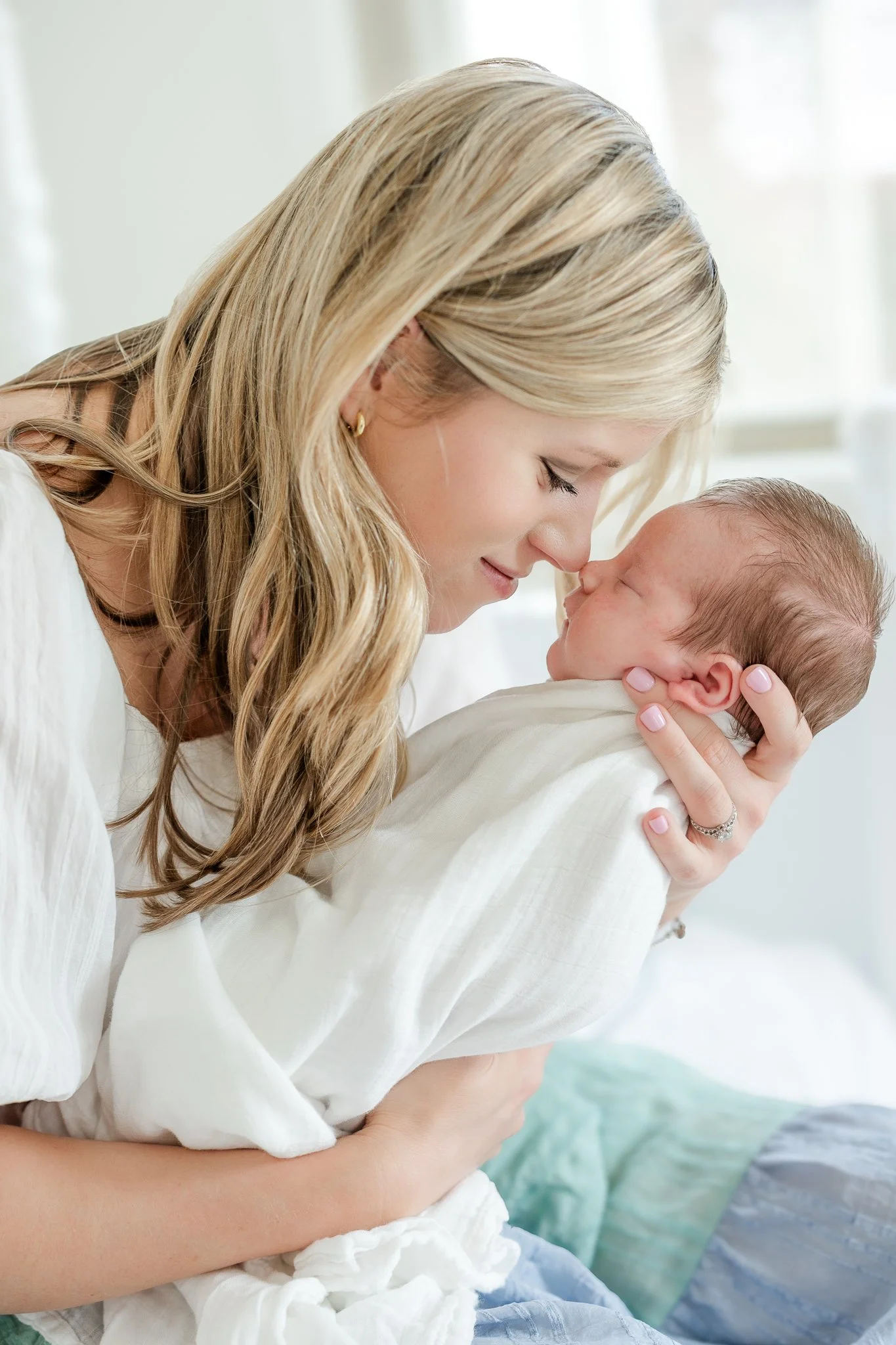Mother holding and nuzzling newborn baby while wrapped in a white blanket.