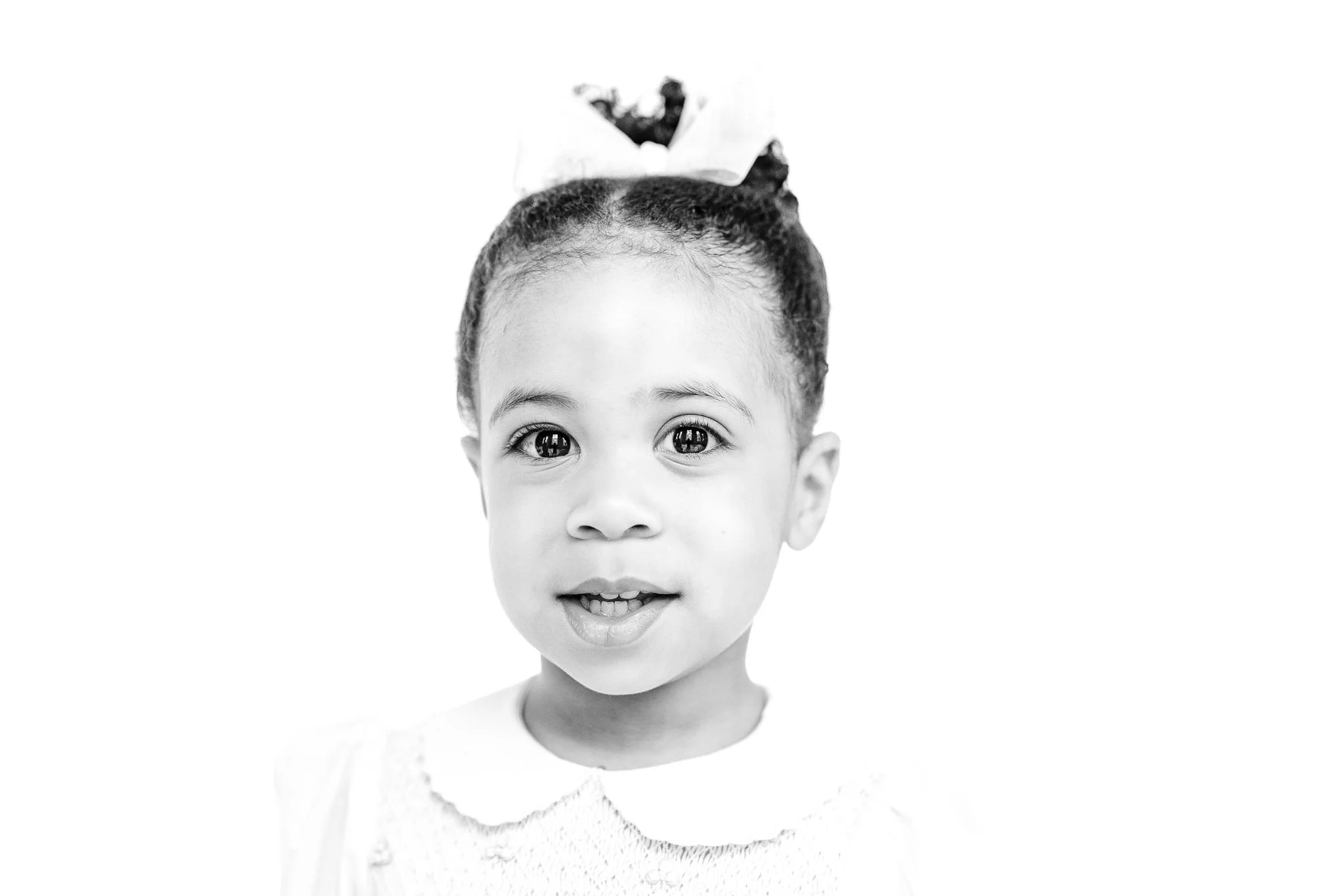 Black and white portrait of a young child with a bow in their hair, wearing a white collared shirt.