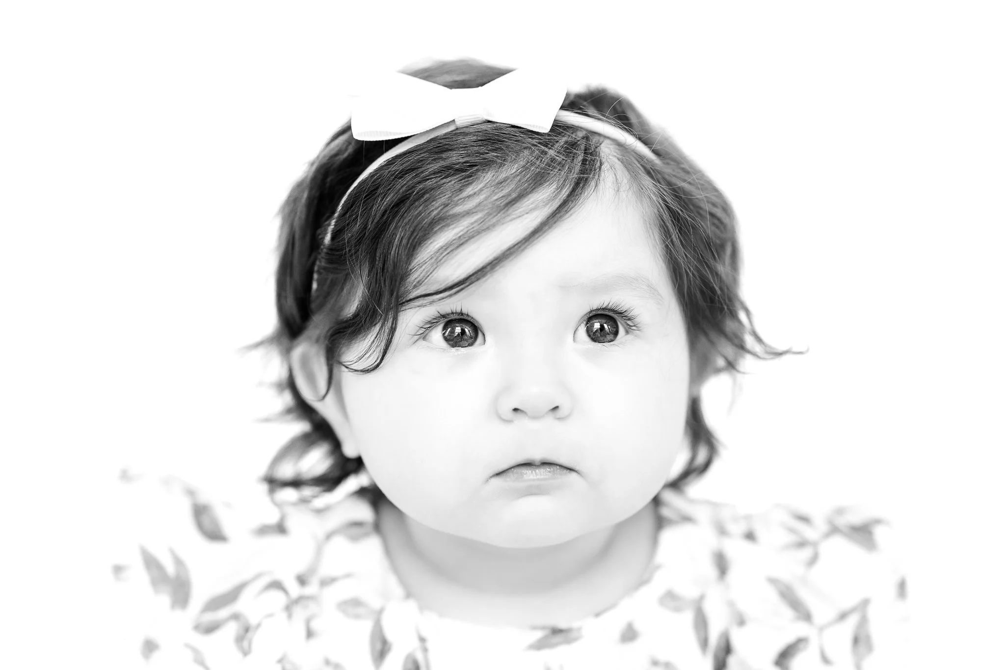 Black and white portrait of a baby with a headband and bow.