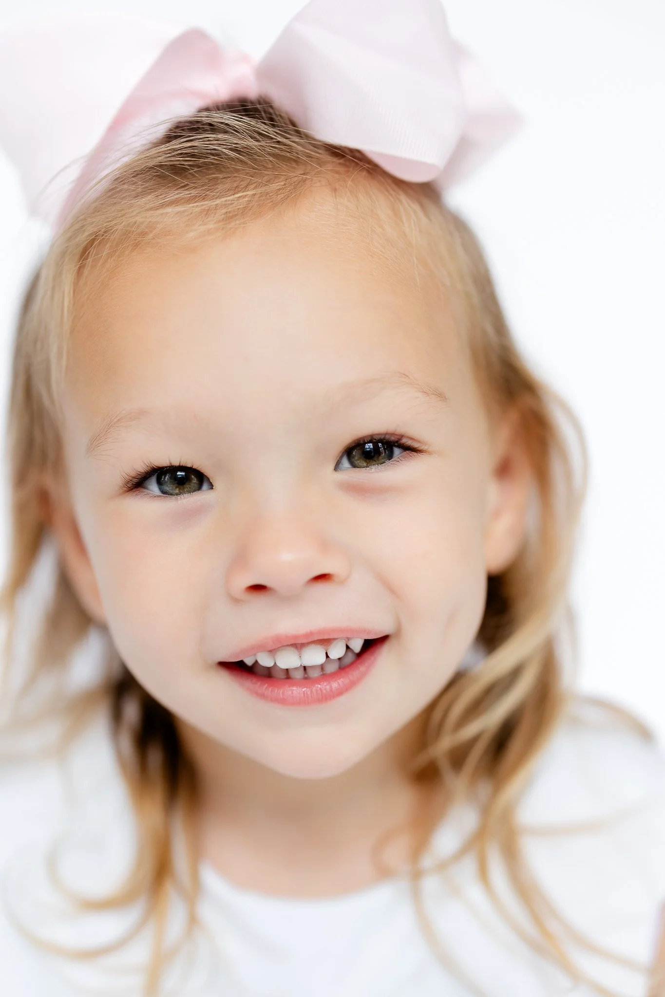 Close-up of a smiling young girl with a pink bow in her hair.