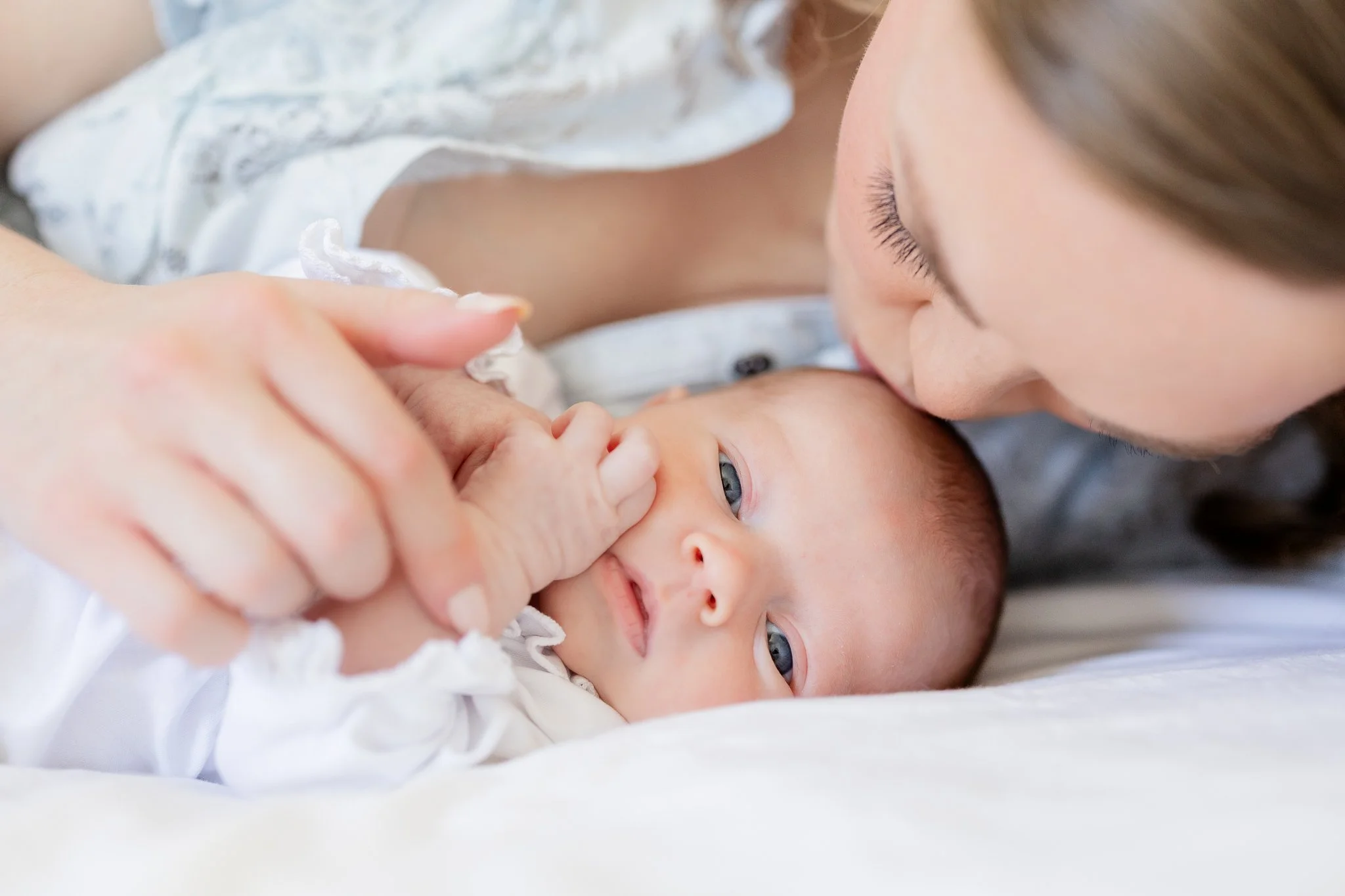 Close-up of a mother gently kissing her newborn baby, who is lying on a white blanket.