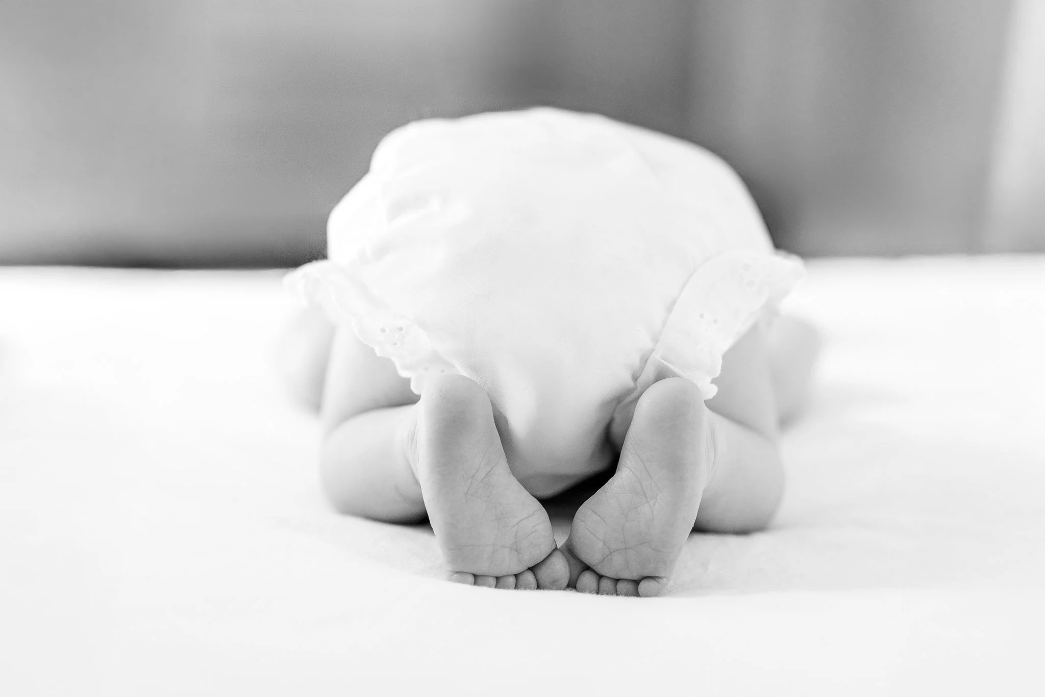 Black and white photo of a baby lying face down, wearing a diaper, showing feet and legs.