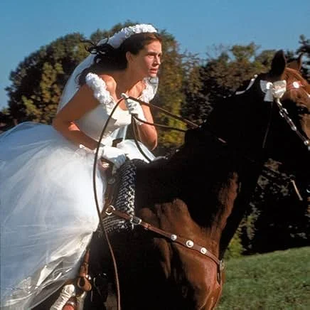 Scene from Runaway Bride showing Maggie riding away on a white horse through a small town — romantic comedy with cozy fall vibes.