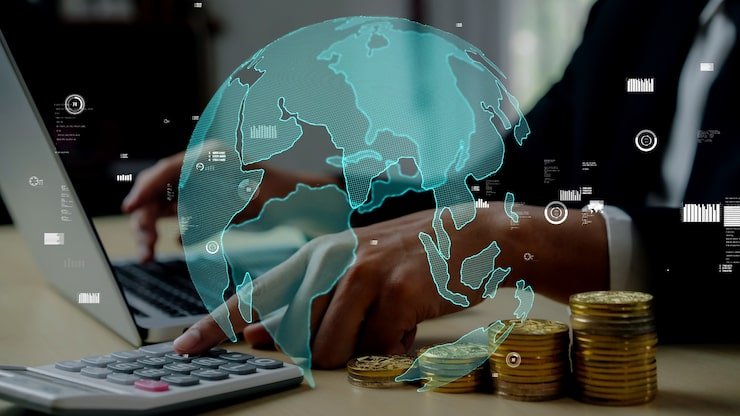 Business person using laptop with digital globe overlay and stacks of coins on table.