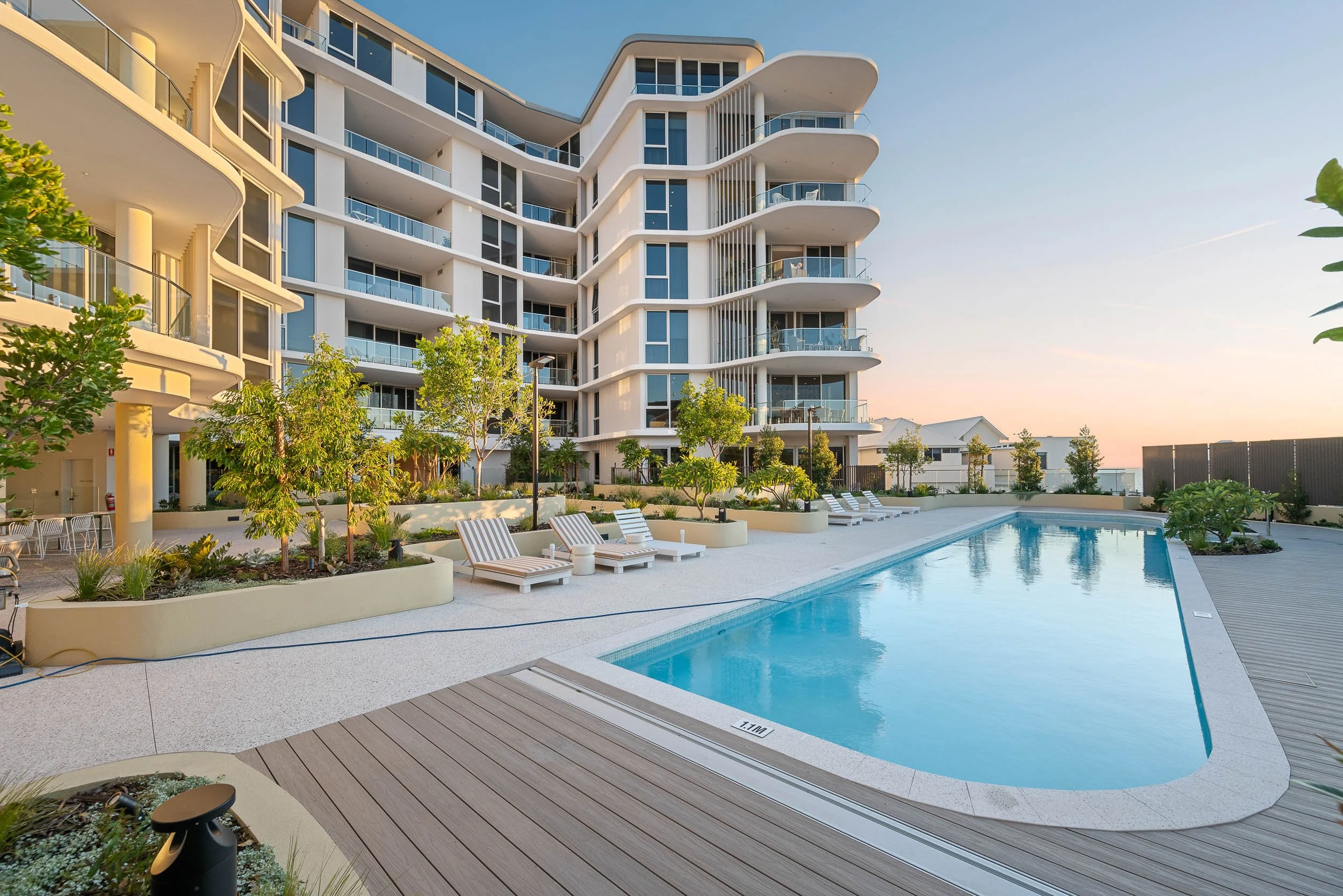 Apartment swimming pool with a curved edge, poolside decking and landscaped surrounds.