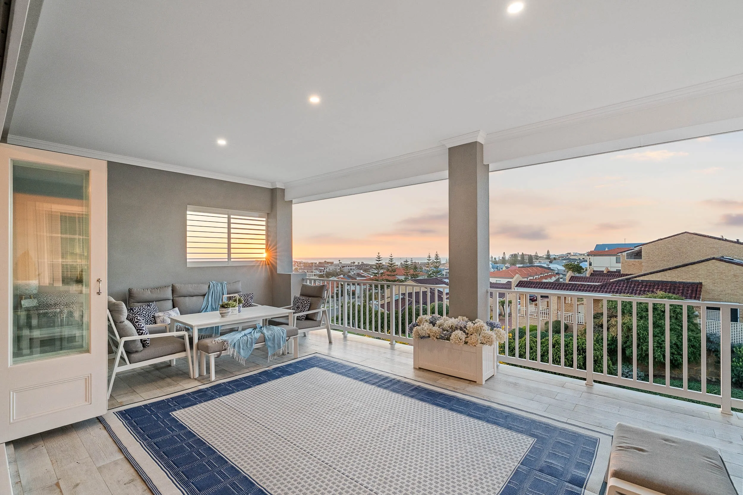 Covered terrace with outdoor seating, a patterned rug and glass balustrades at dusk.