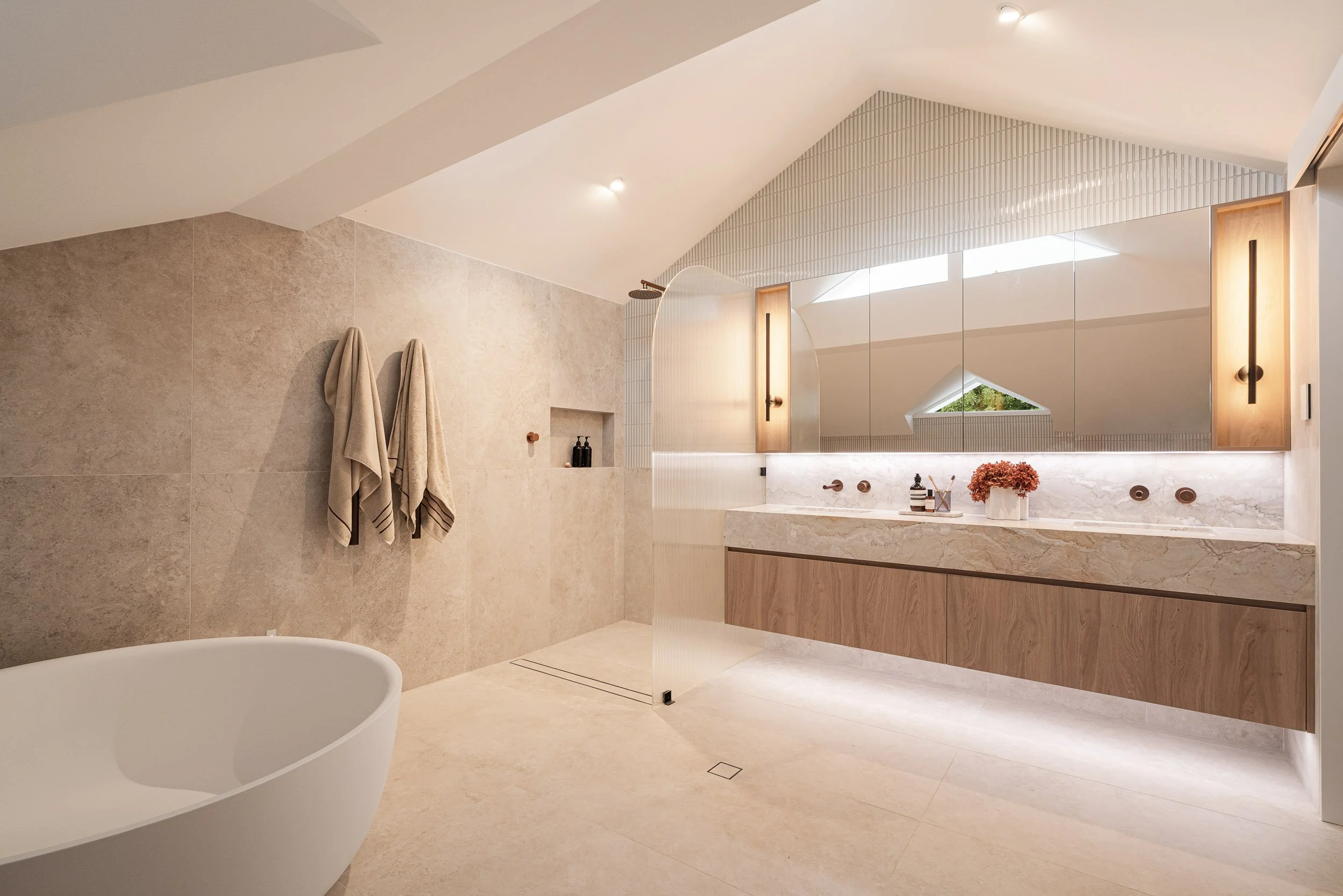 Bathroom with a long floating vanity, wide mirror and softly lit beige finishes.